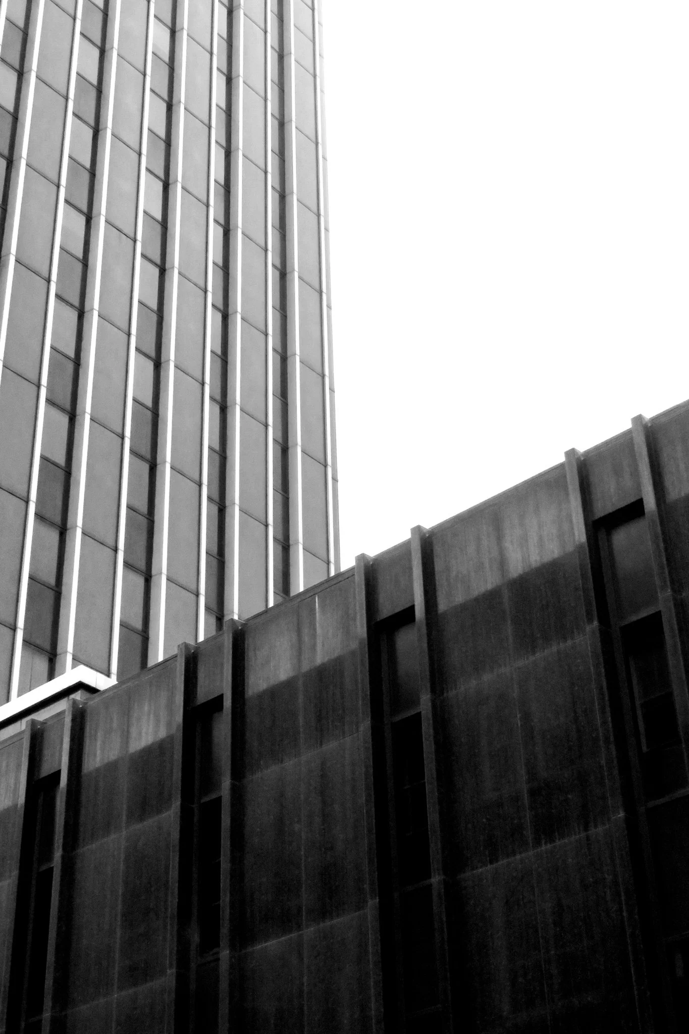 A black and white photograph of a tall building with glass windows on the left side and concrete structures on the right side.