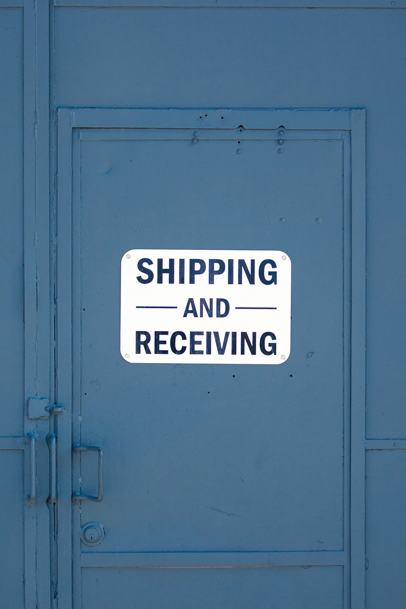 Blue door with a partial sign reading 'SHIPPING AND RECEIVING' at the bottom.