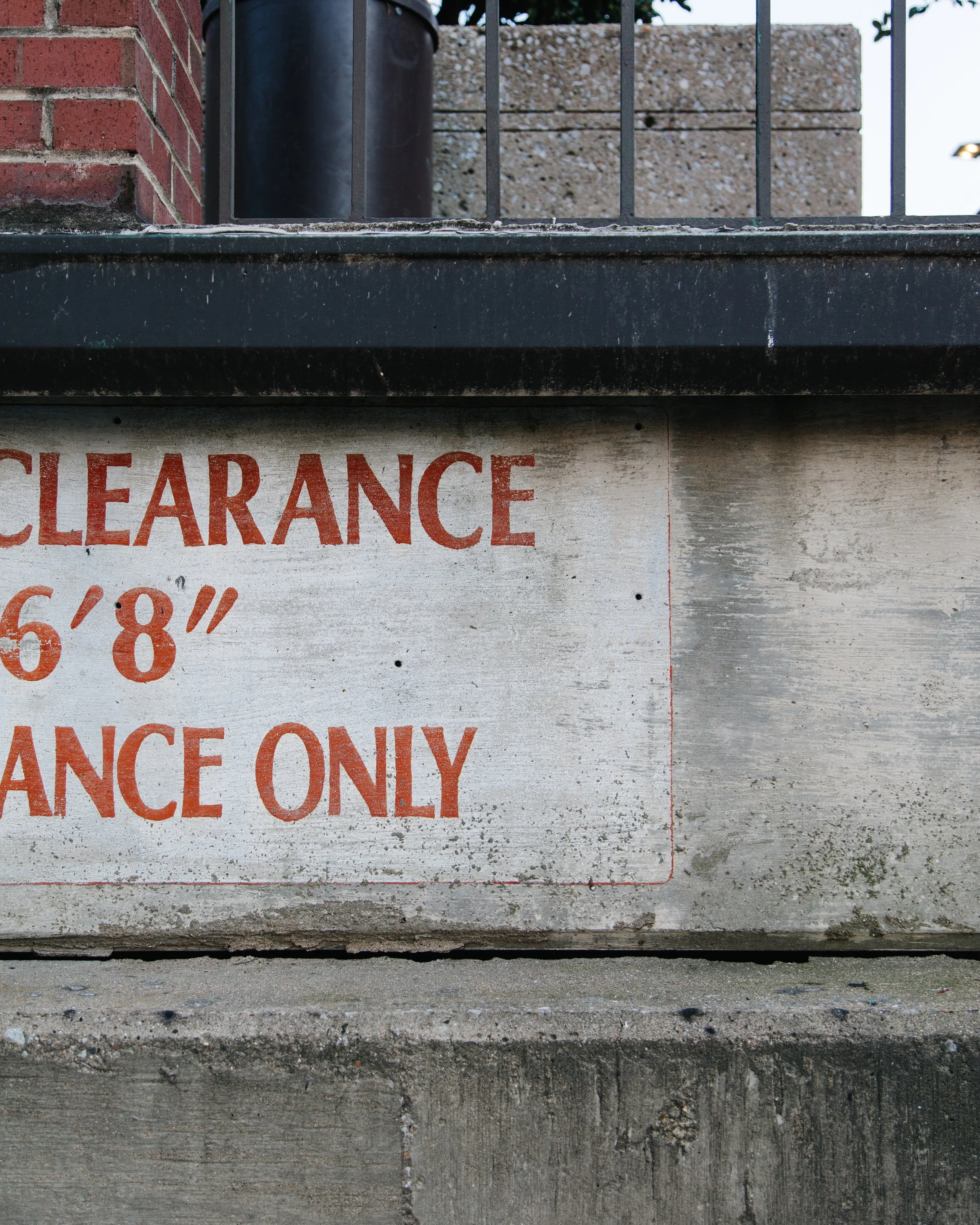 Close-up of a concrete sidewalk beneath a metal step with a weathered sign that has red text reading 'CLEARANCE' and additional red text that is partially visible.