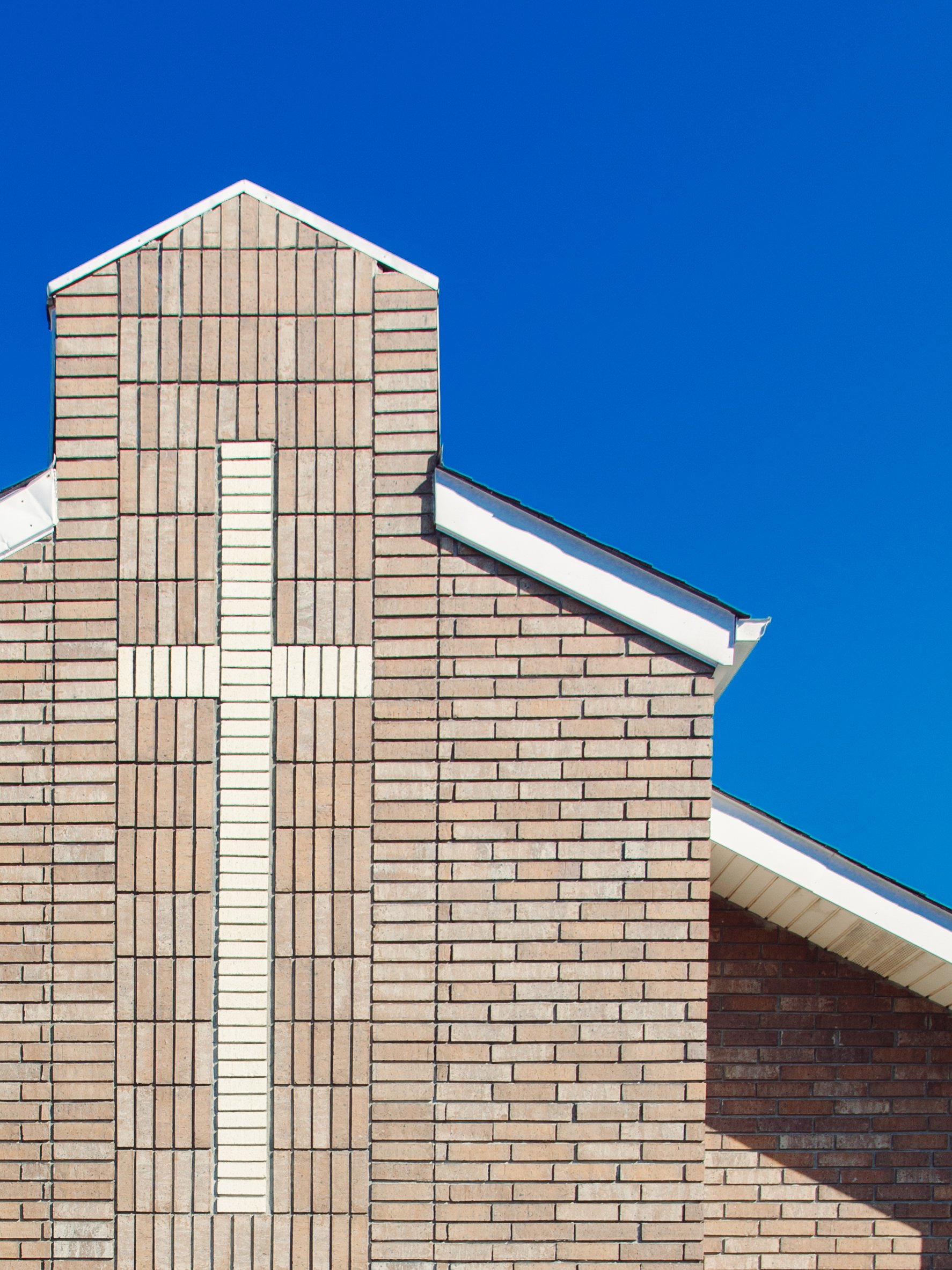 Close-up of a brick house with a gabled roof and a vertical decorative brick pattern on the wall, against a clear blue sky.