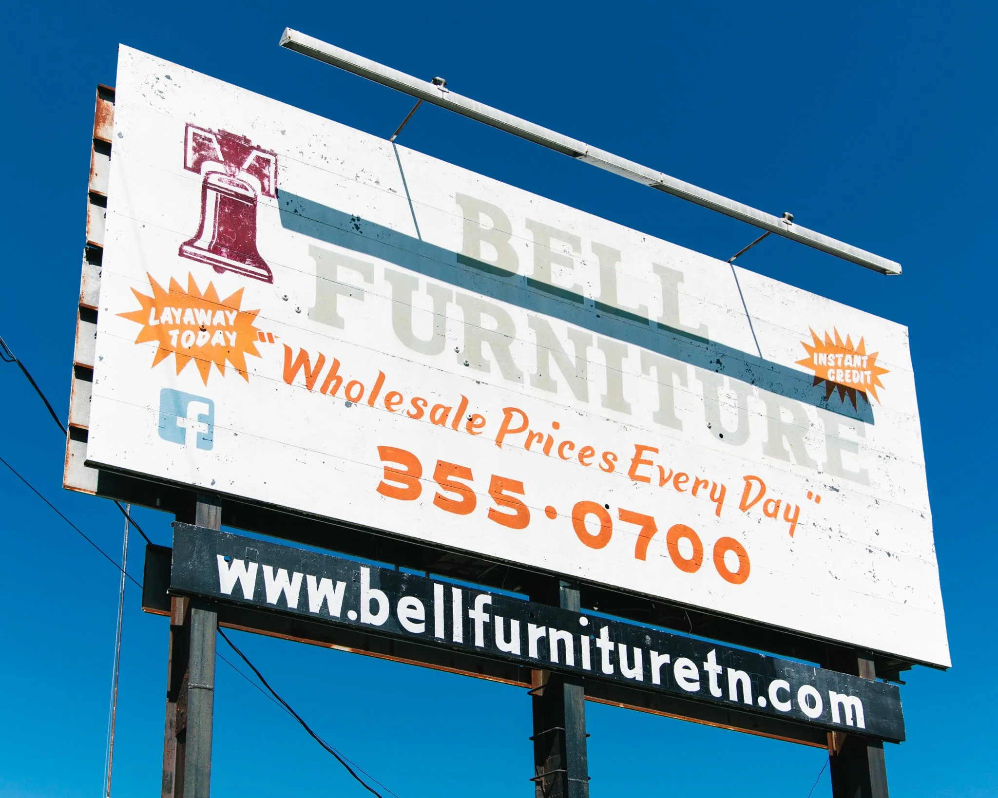 Outdoor sign advertising wholesale prices, instant credit, and furniture store website, with a blue sky background.