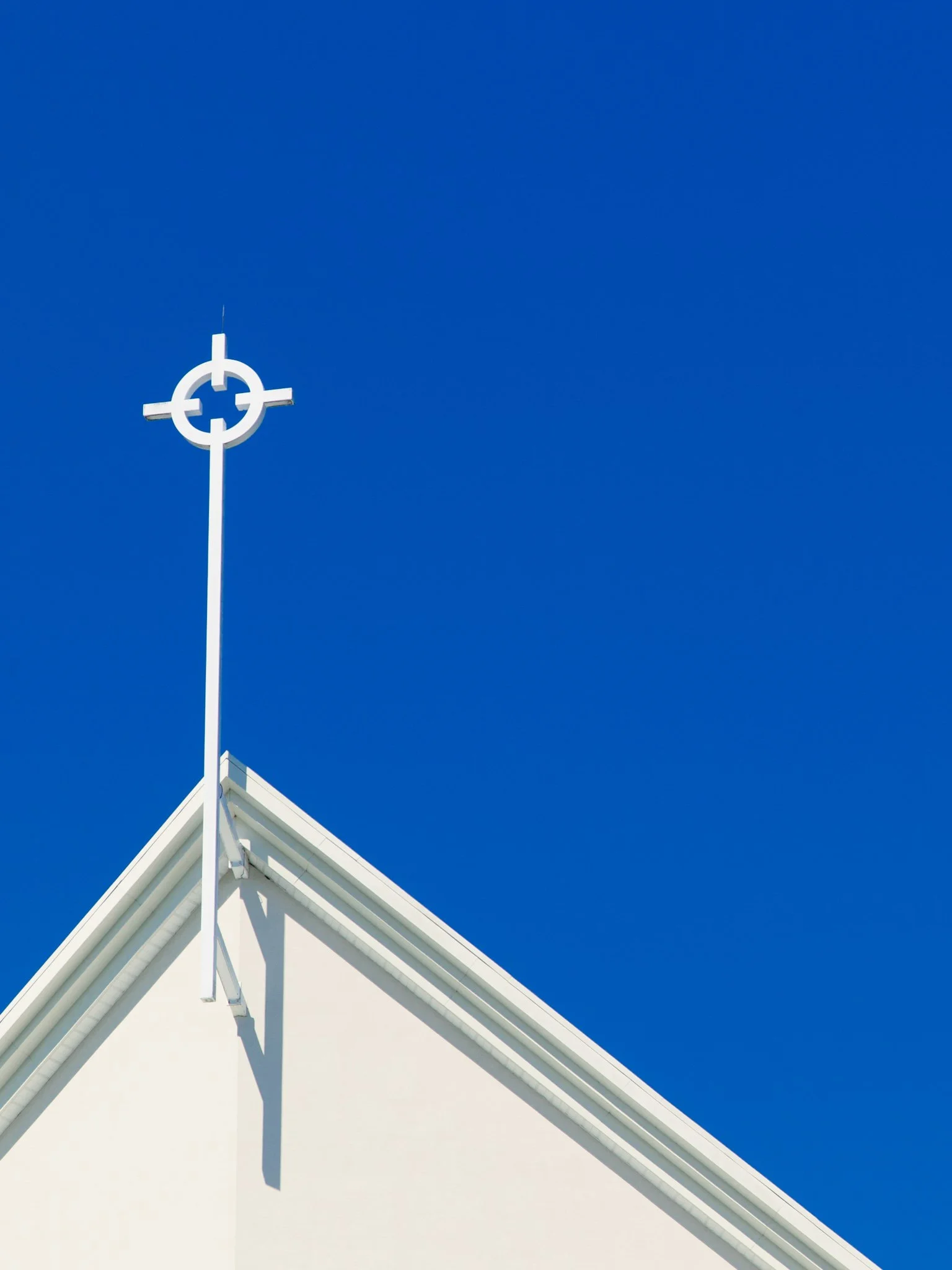White church steeple with a cross-shaped weather vane on top, set against a clear bright blue sky.