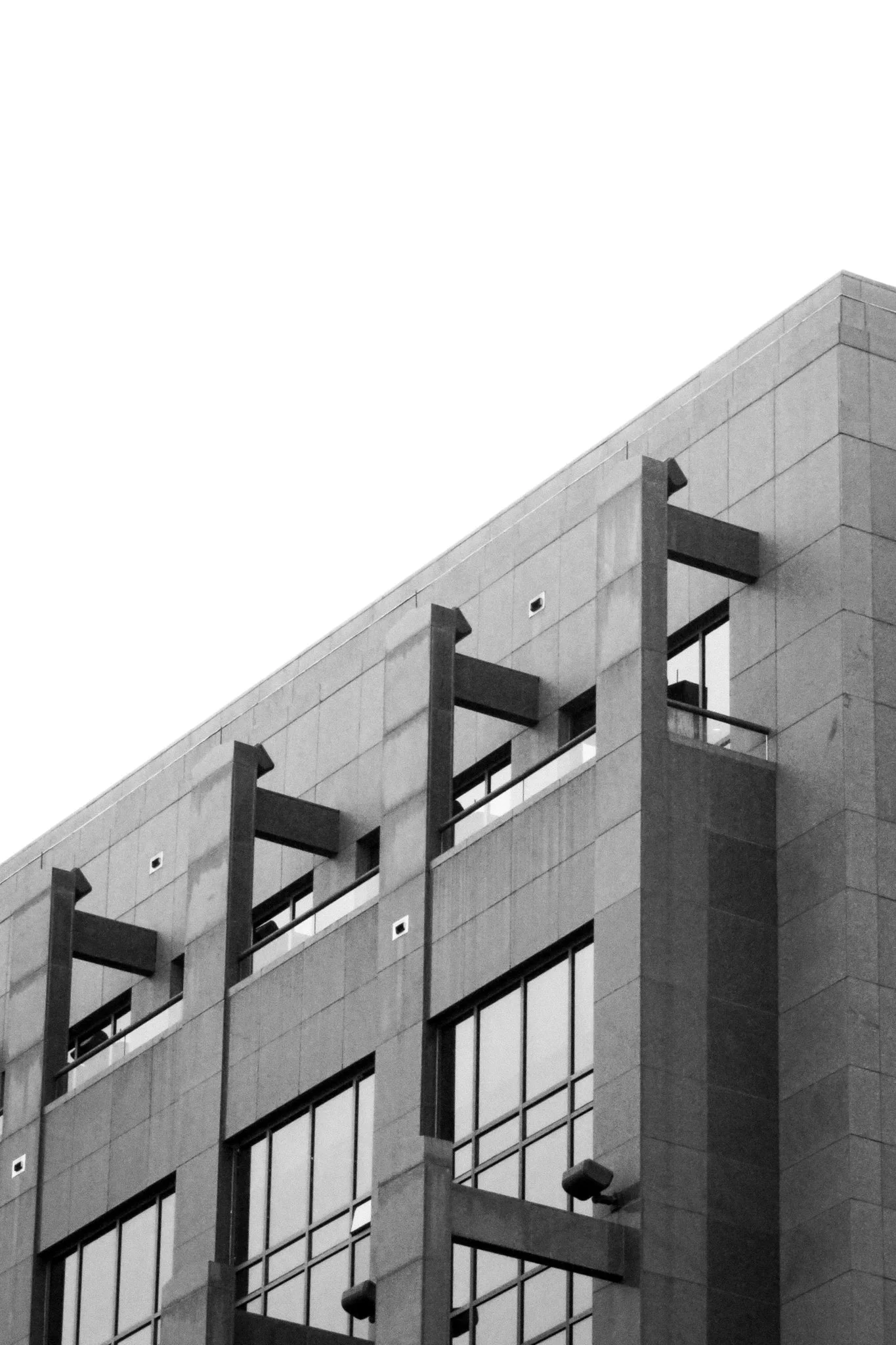 Close-up of a modern multi-story office building with glass windows and concrete walls, featuring vertical architectural elements and some visible balcony spaces.