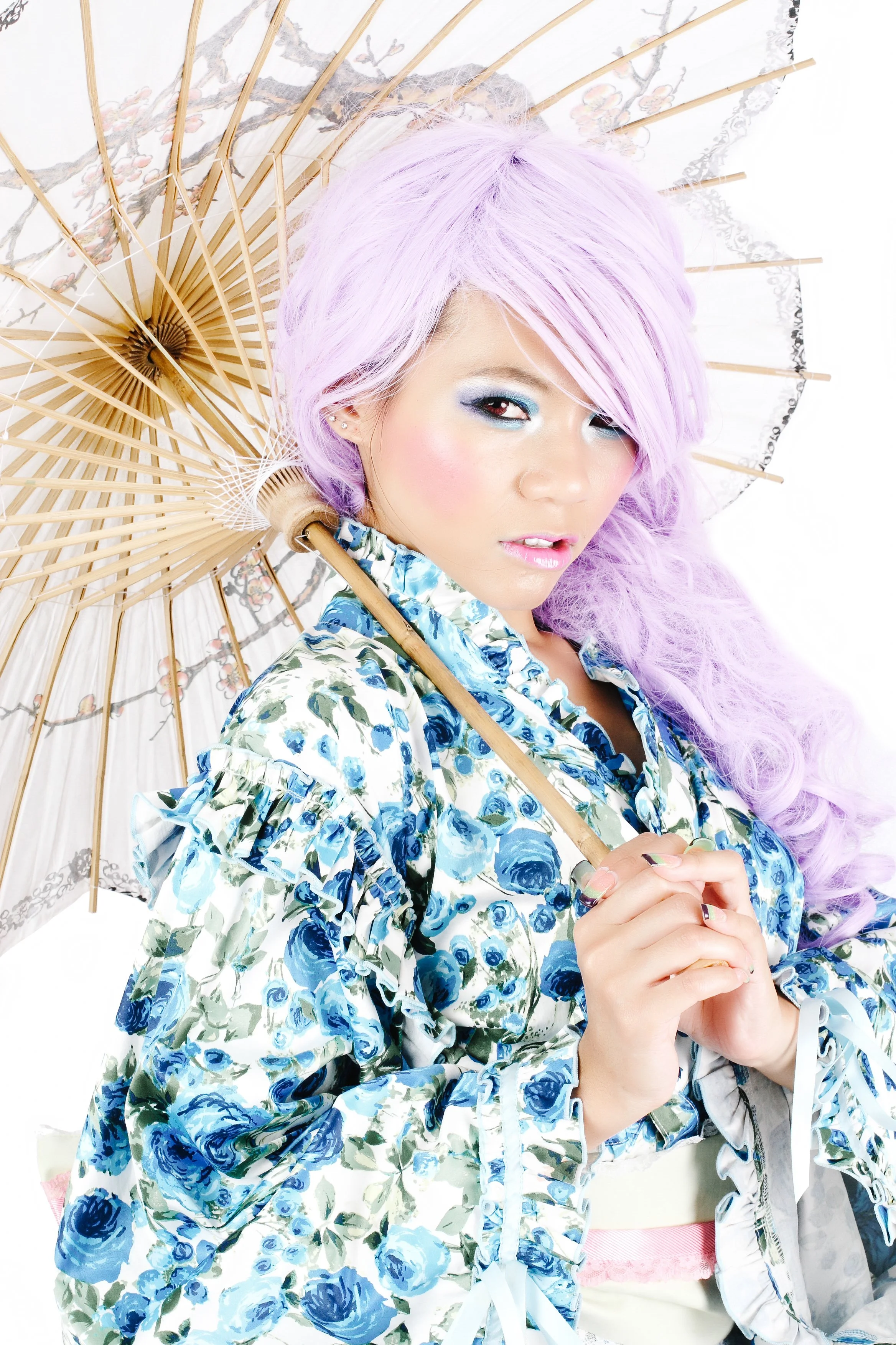 Woman with pastel purple hair wearing a blue and white floral jacket holding a paper parasol with cherry blossom design.