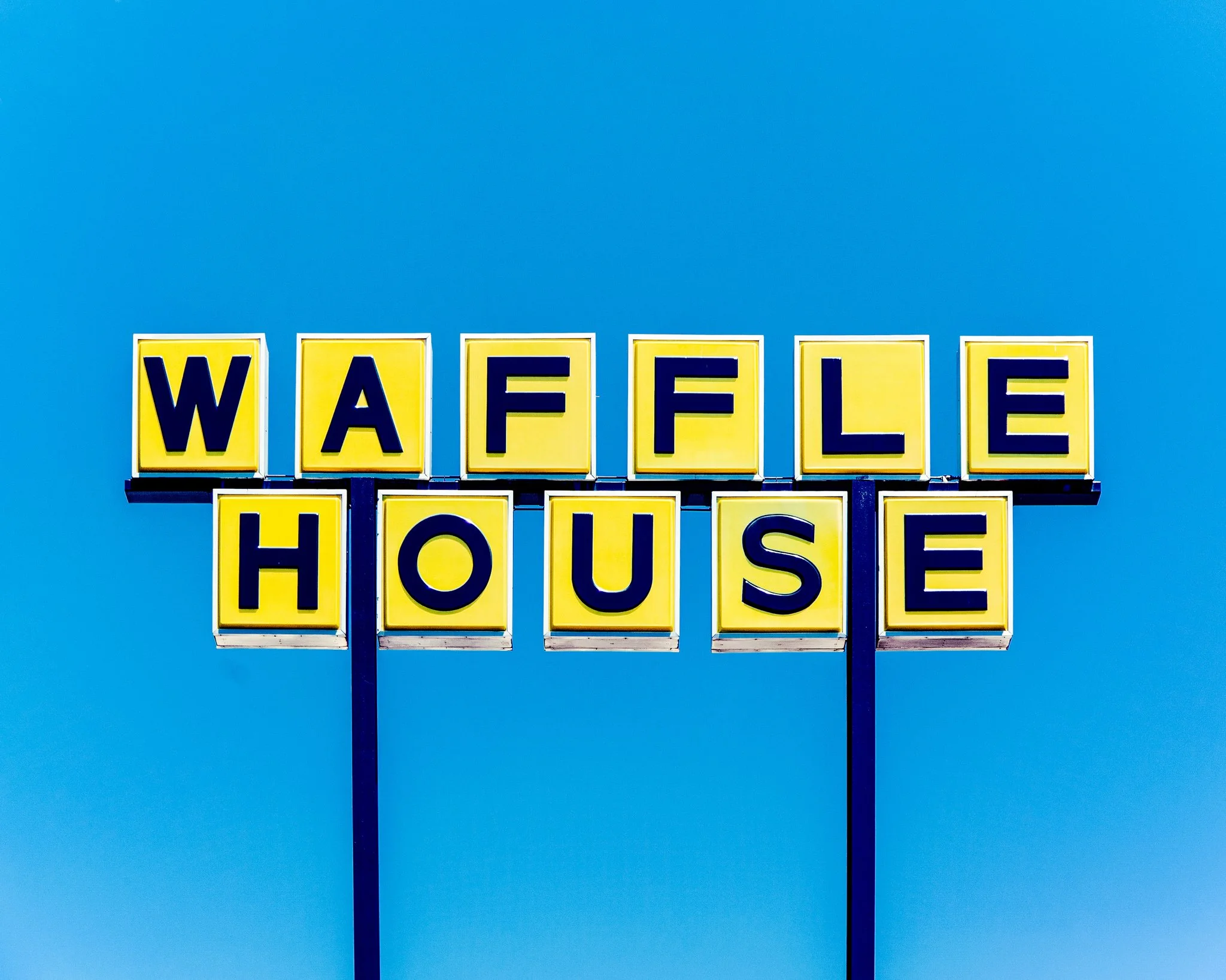 Yellow sign with black letters spelling out 'WAFFLE HOUSE' against a clear blue sky.