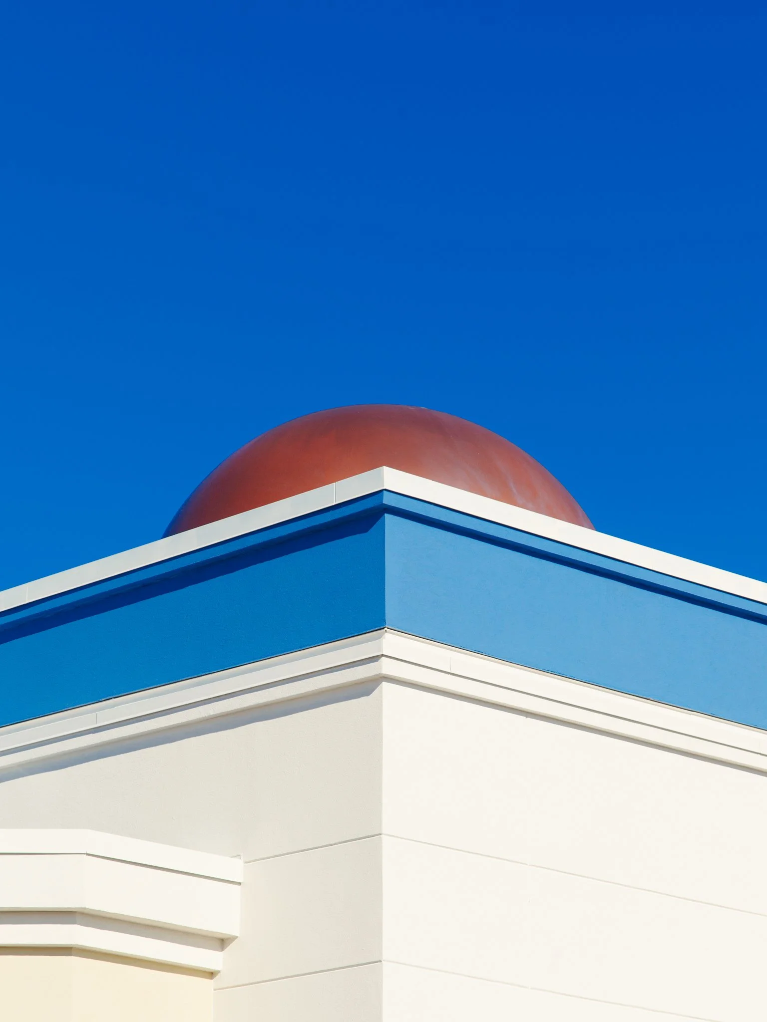 Close-up of modern architectural building with rounded red dome, sharp white and blue angular design, beneath a clear blue sky.