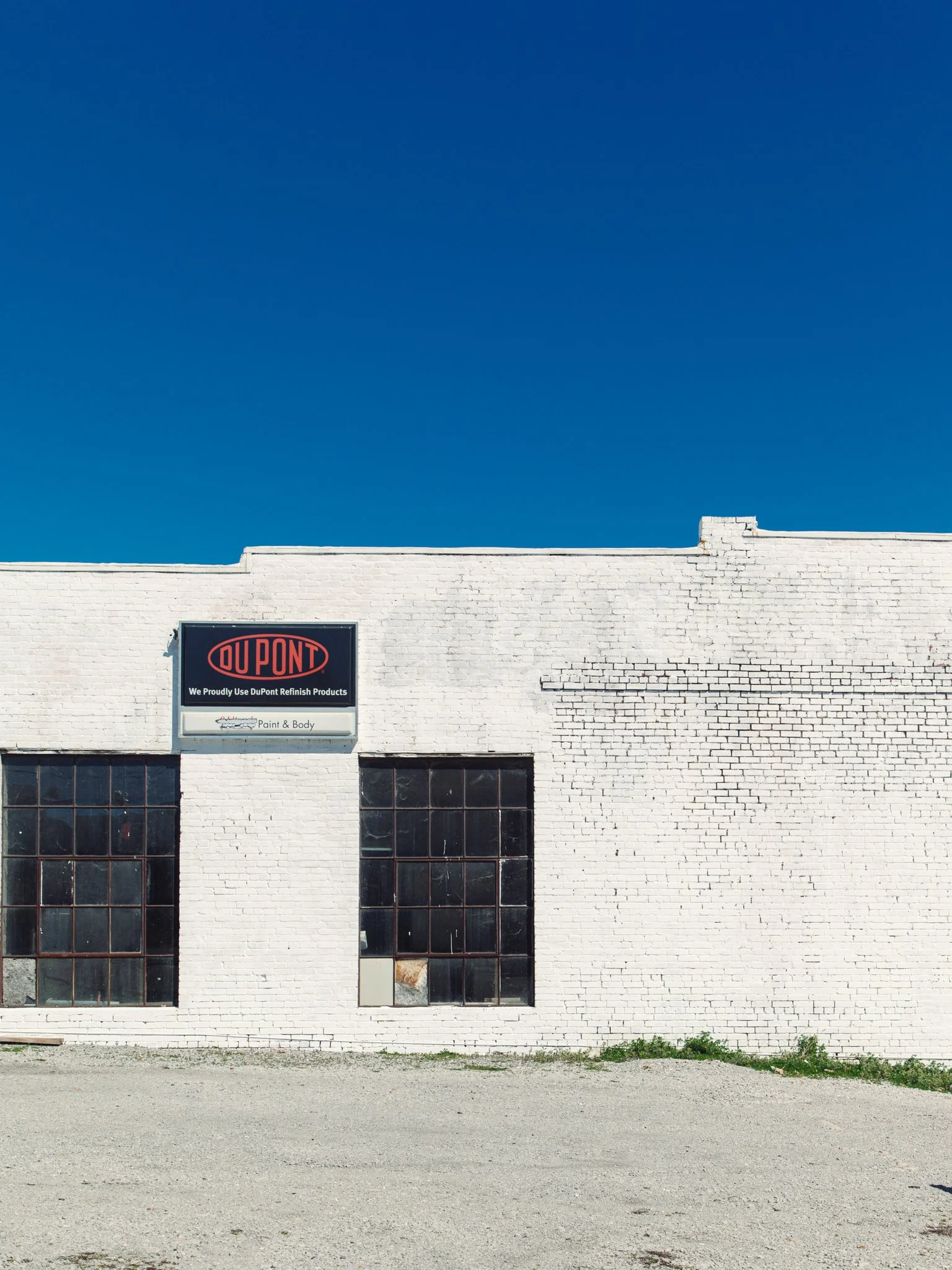 White brick building with large industrial-style windows, a sign for DuPont on the wall, and a clear blue sky above.