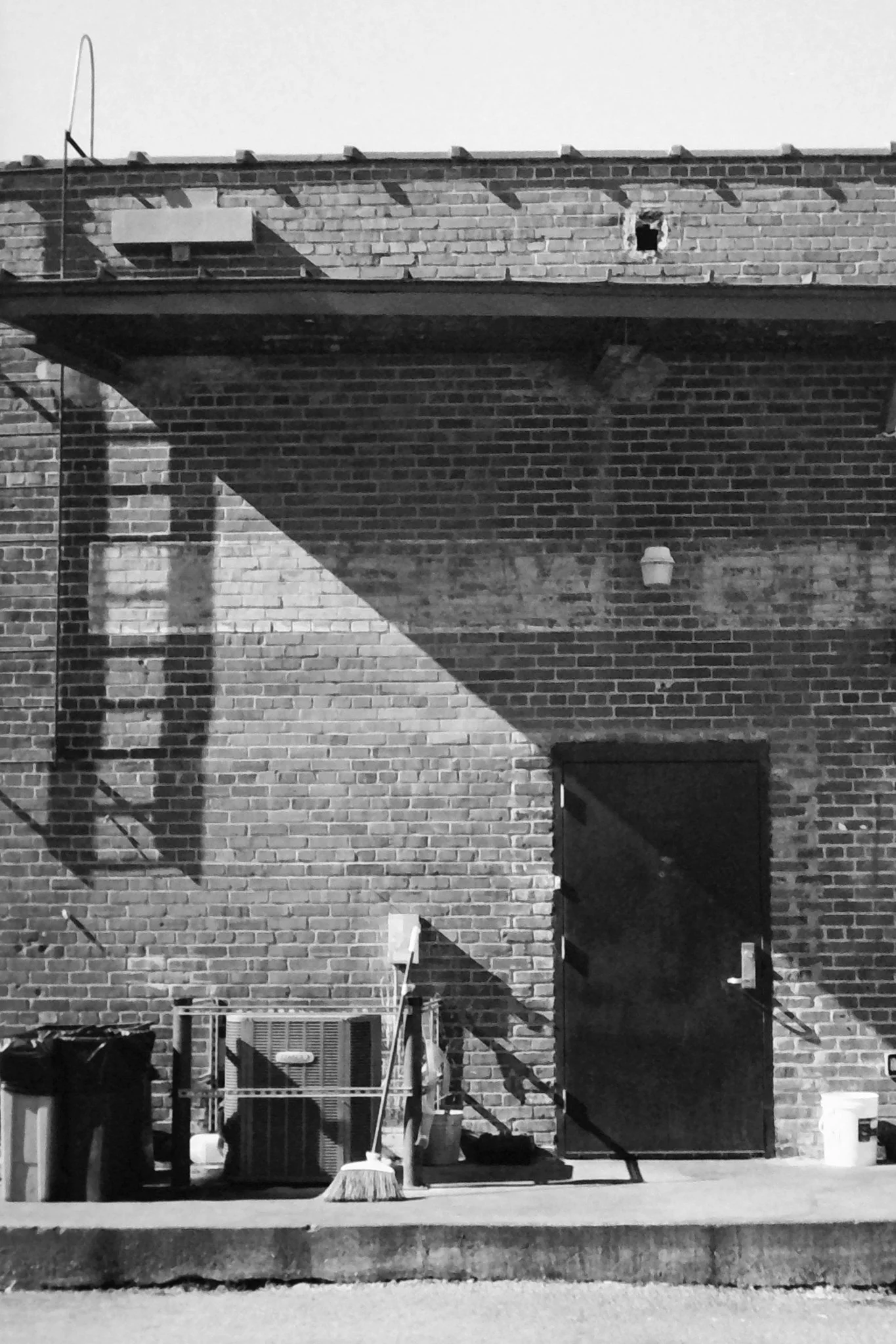 Backyard scene with brick wall, open door, outdoor supplies, and cleaning tools in black and white.