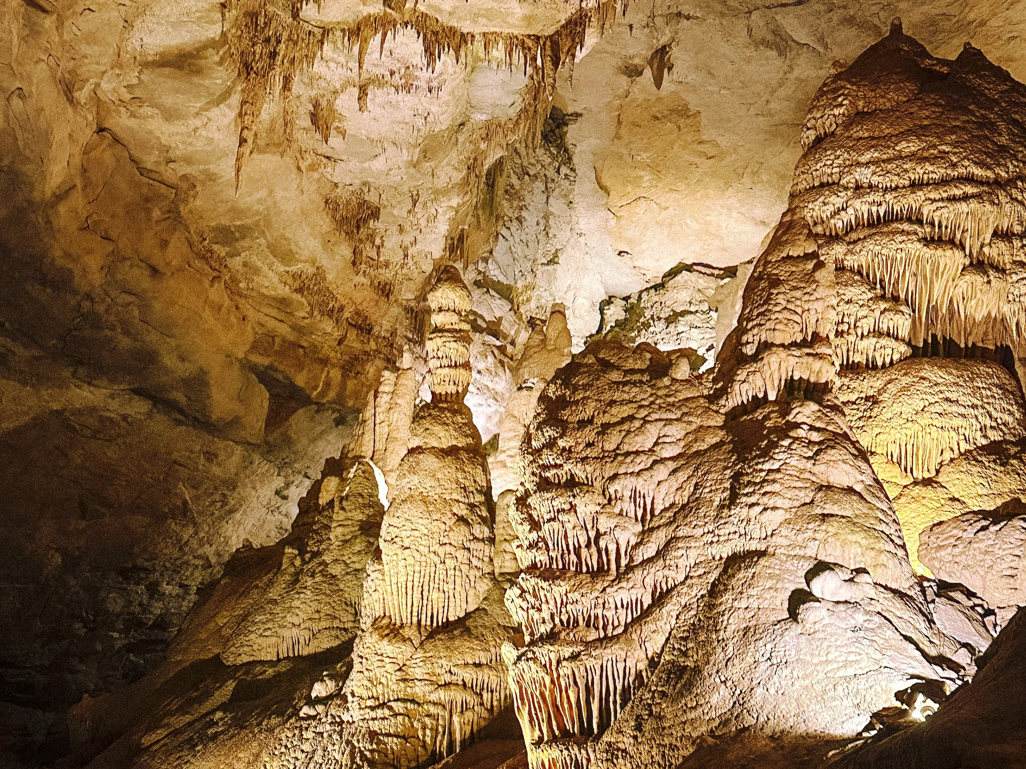 Inside a cave with stalactites hanging from the ceiling and stalagmites rising from the ground, illuminated by warm lighting.