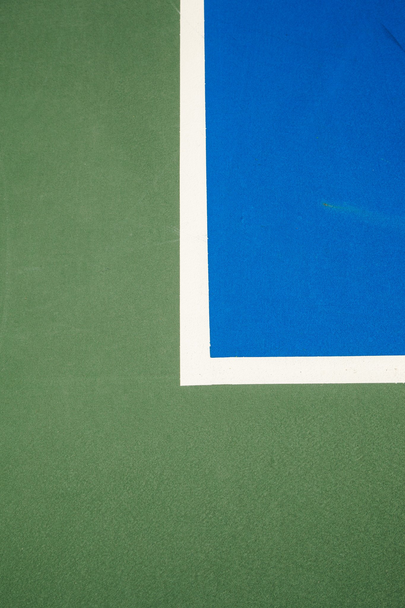 Close-up of a blue and green tennis court with a white boundary line.