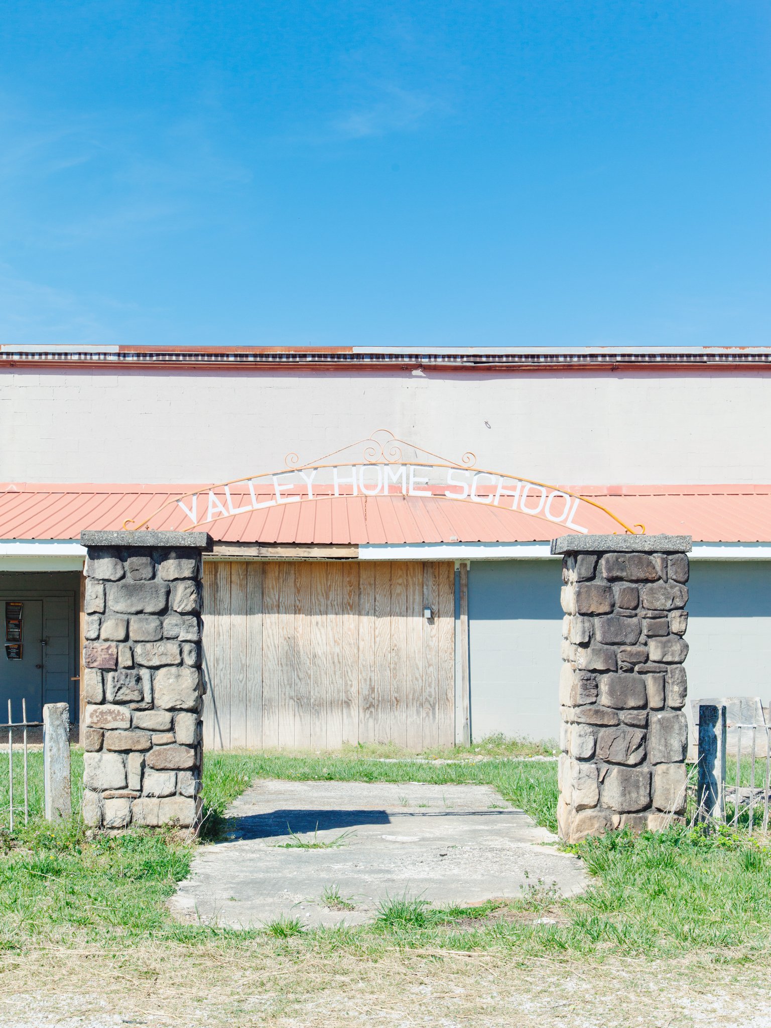 Front of Valley Home School building with stone columns and a pink roof, set against a bright blue sky.