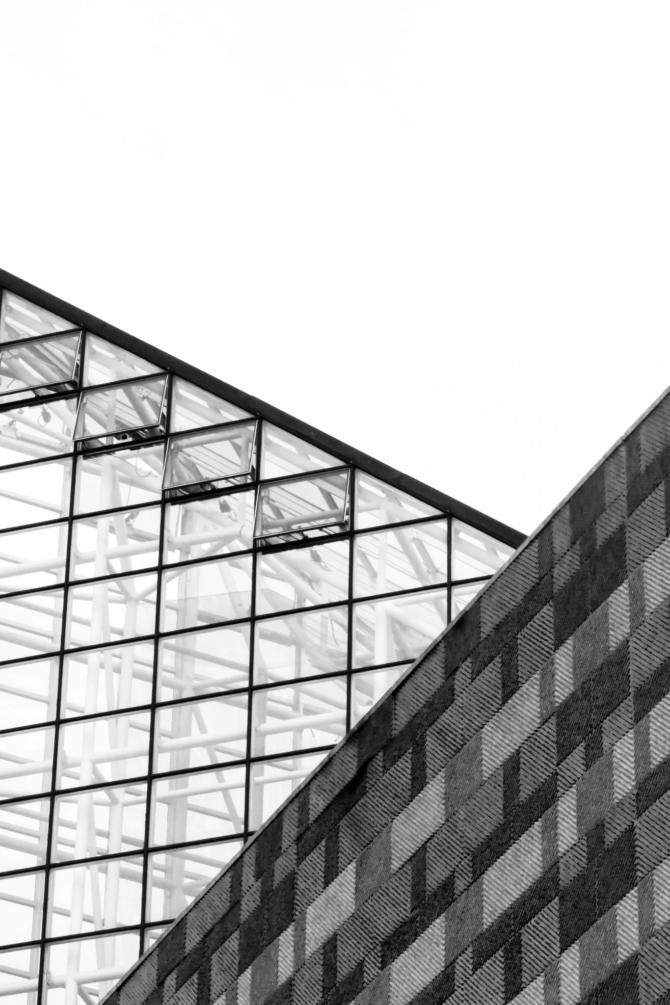 Black and white photo of modern building with glass windows and textured sloped wall, taken from a low angle.