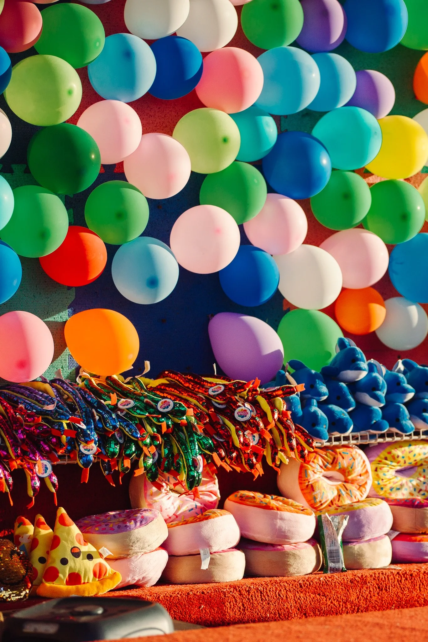 Colorful balloons stacked inside a store display, with plush animal toys and items on a lower shelf.