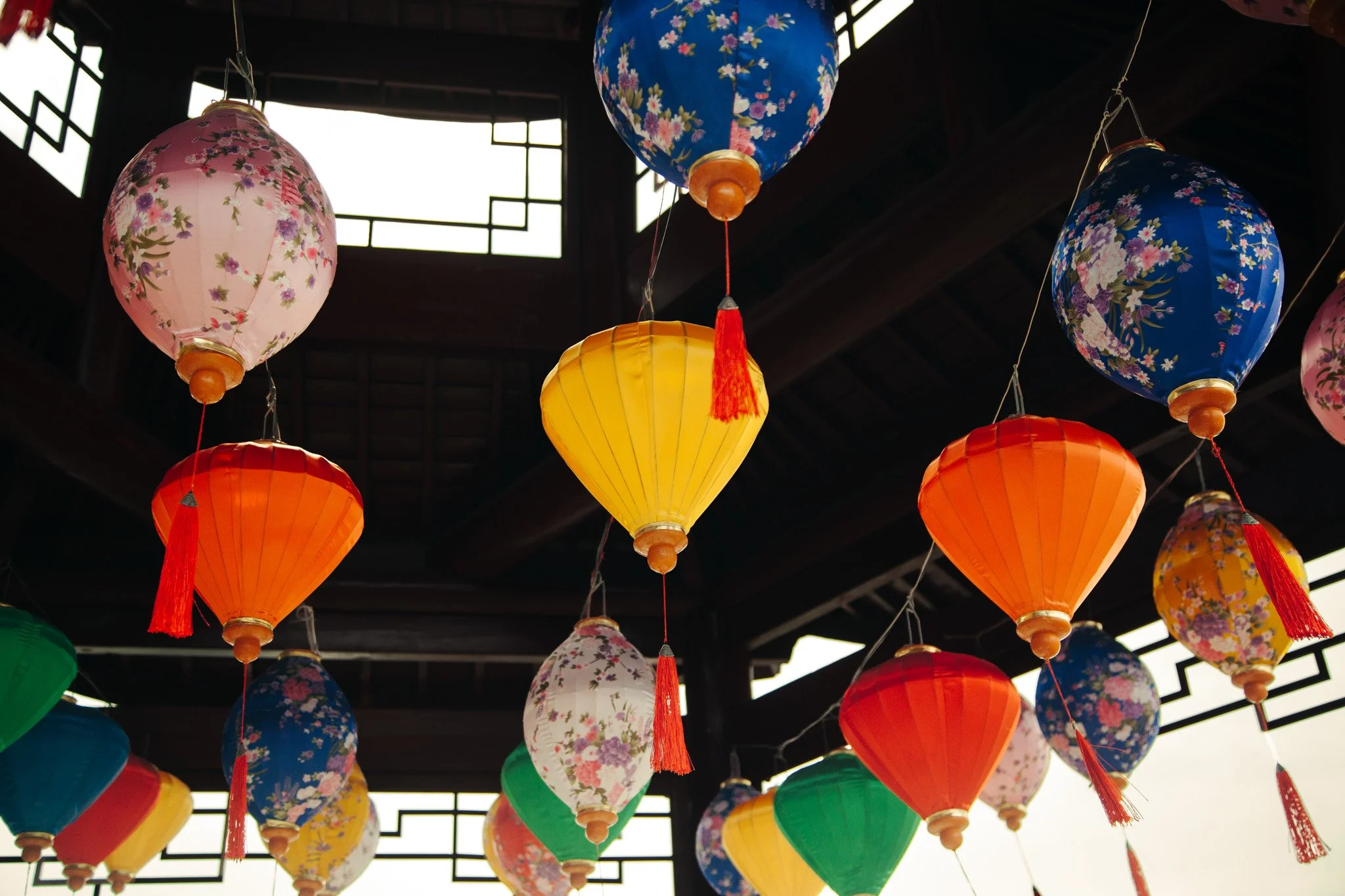 Colorful paper lanterns with floral and geometric patterns hanging from a dark ceiling.