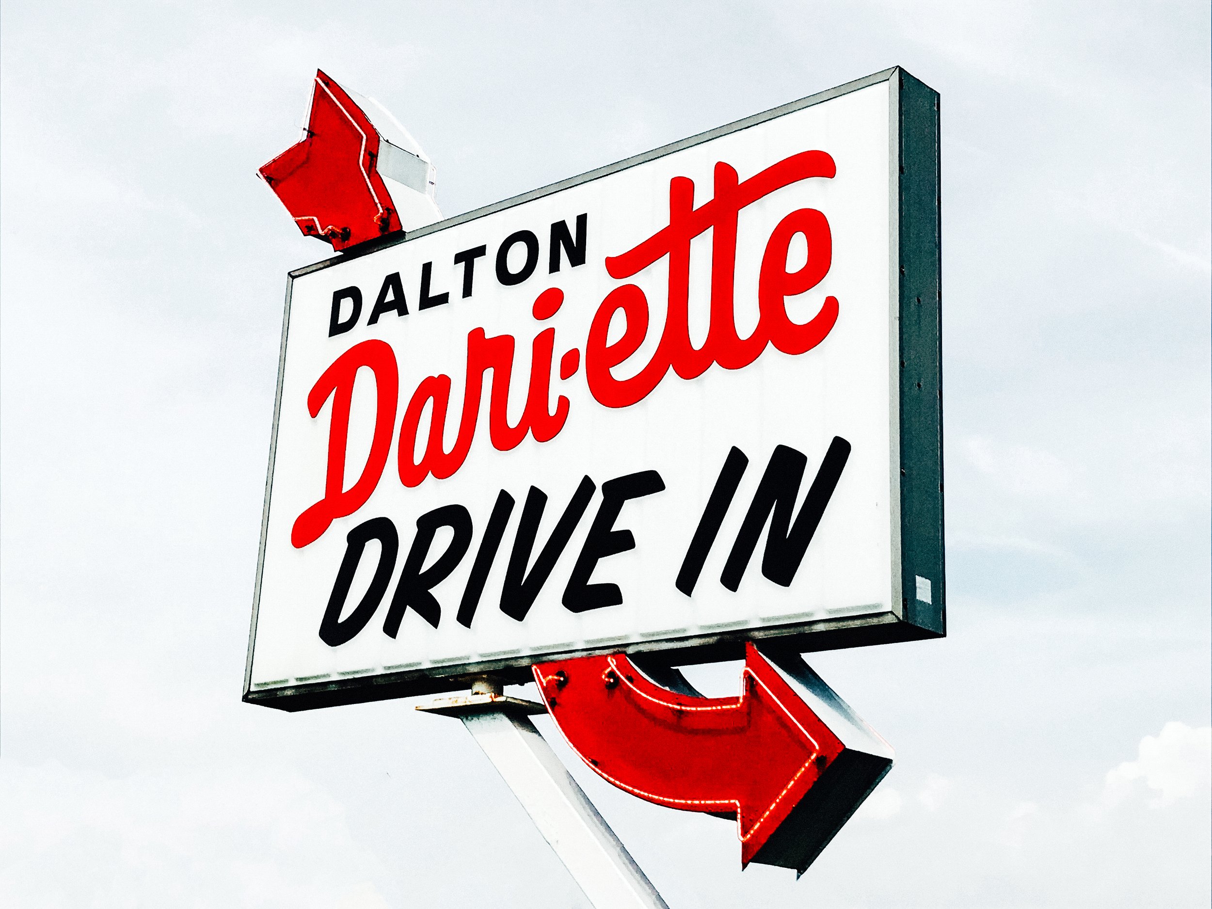 Chevron sign advertising Dalton's Dailies, a drive-in business, with a red arrow and white background