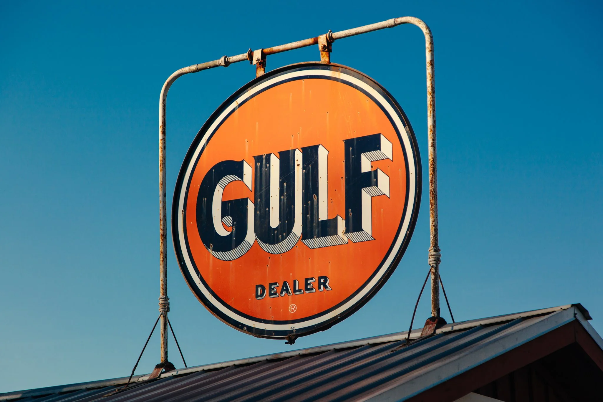Vintage orange and white circular sign with the words 'CULT' and 'DEALER' mounted on rusty metal poles against a clear blue sky.