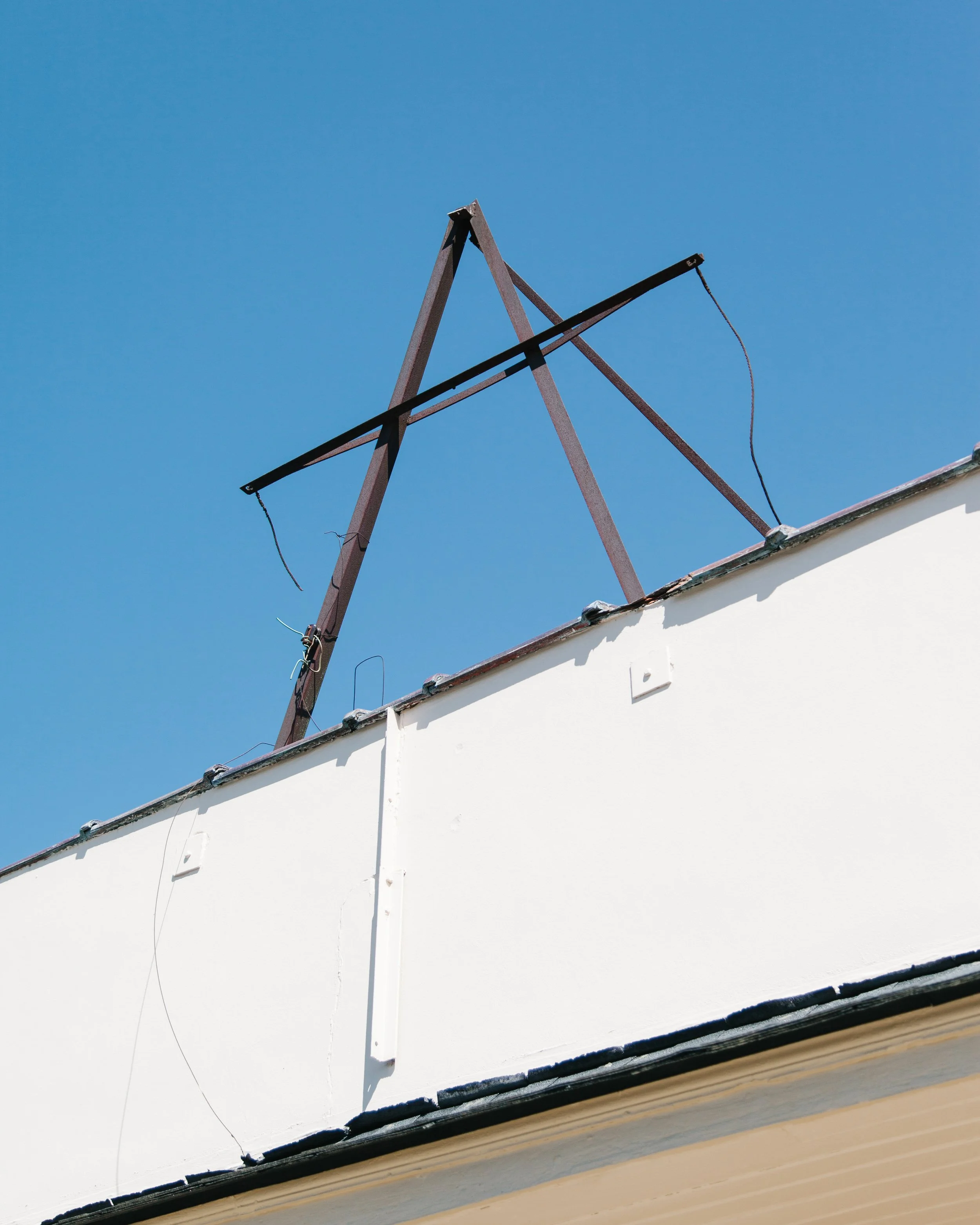 Close-up of a partially dismantled rooftop with metal beams and wiring against a clear blue sky.