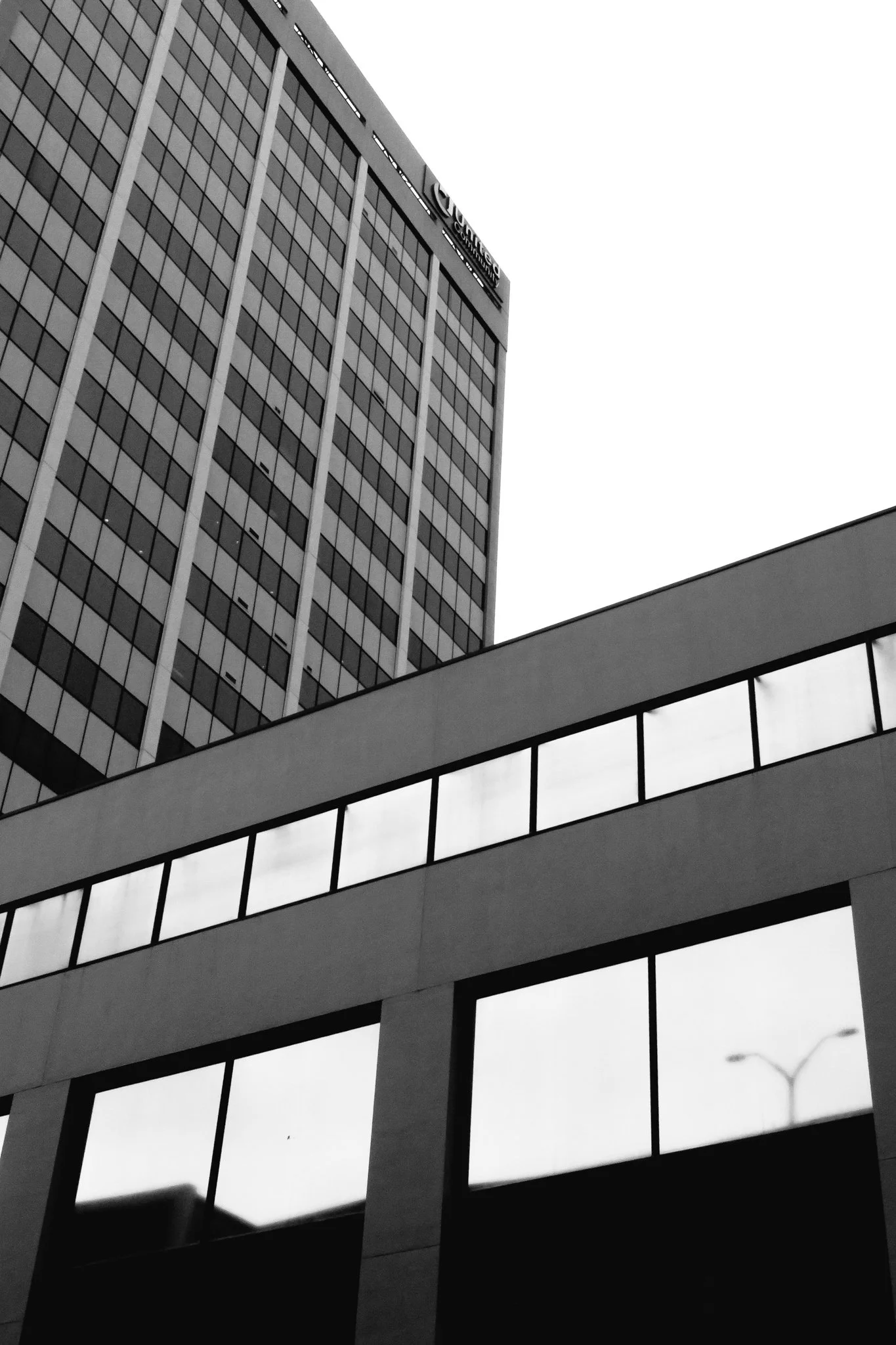 Black and white photo of a modern high-rise office building with many windows and an overhanging balcony or walkway in the foreground.