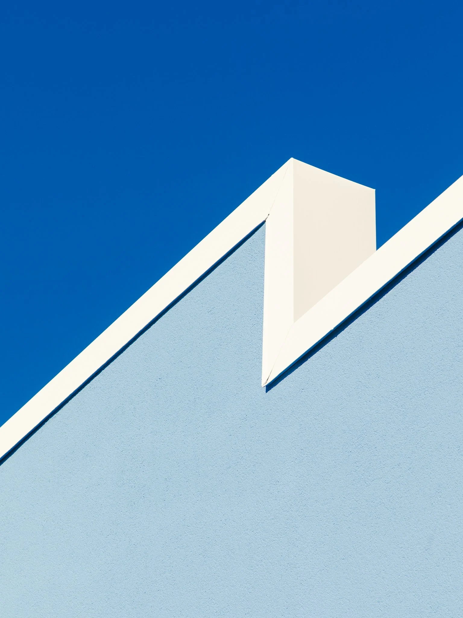 Close-up of a modern building's blue wall with white and light blue trim against a clear blue sky.