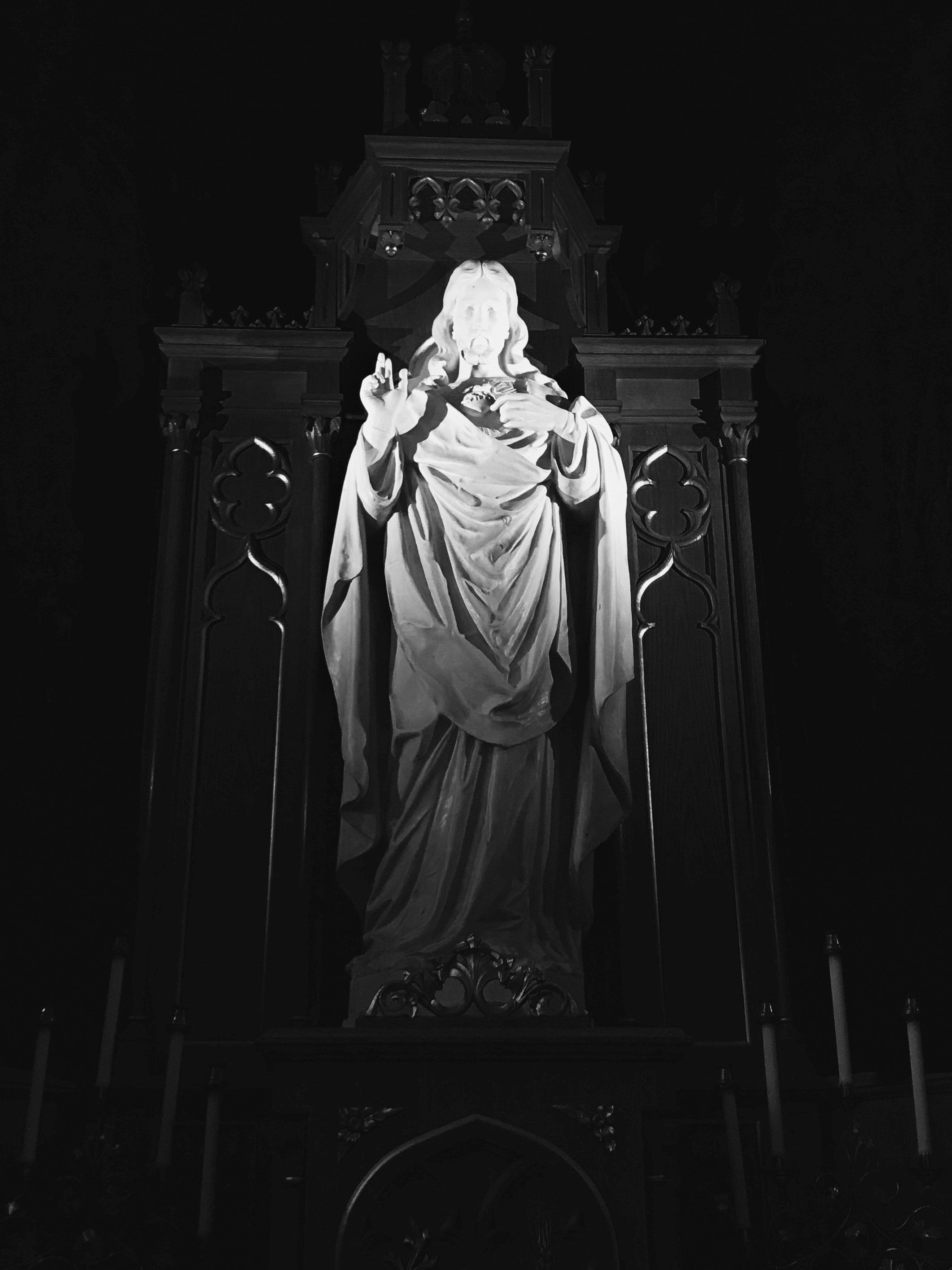A black-and-white statue of Jesus Christ depicted with a sacred heart, standing on an ornate platform with decorative gothic-style arches.