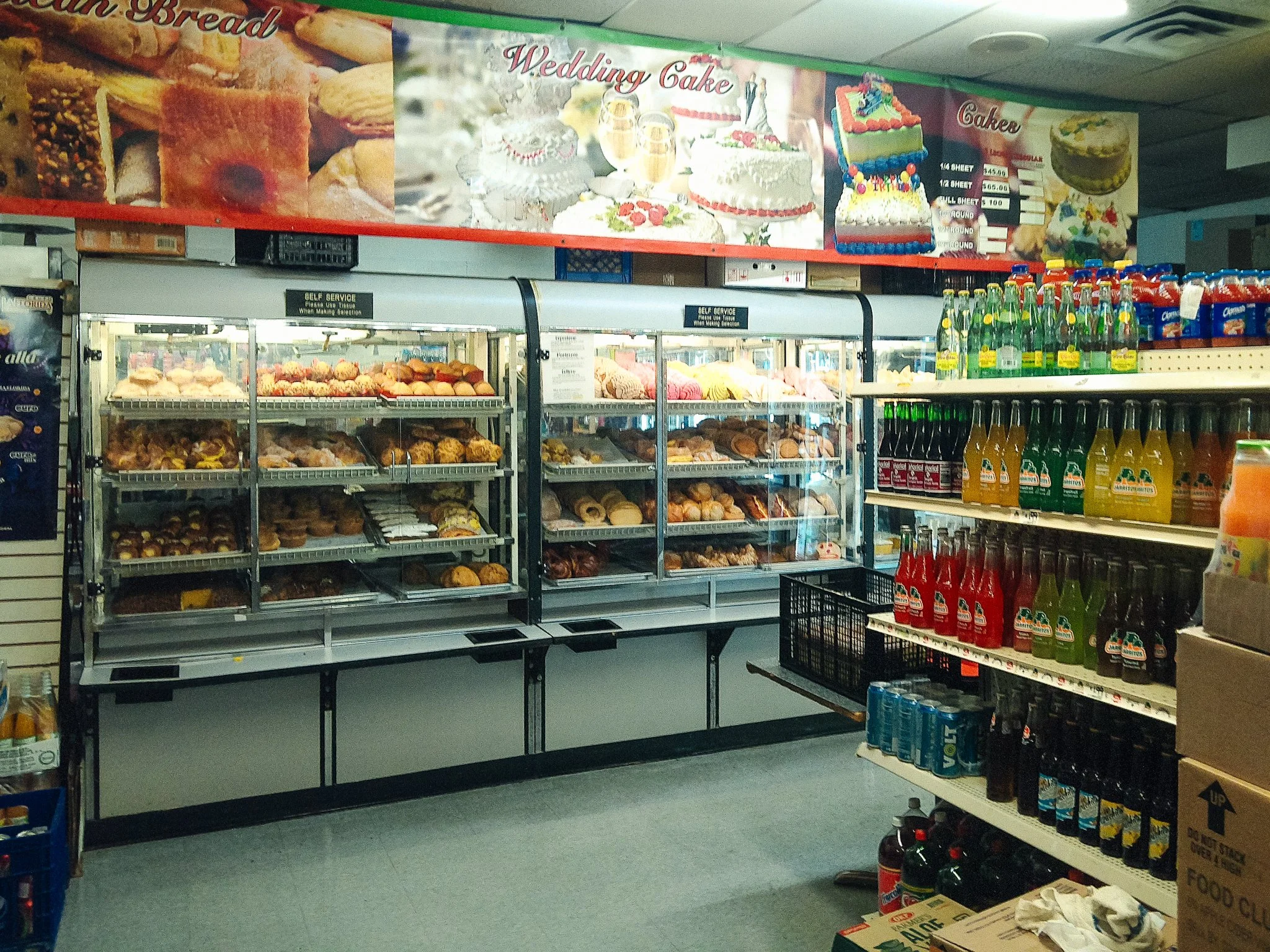 Grocery store aisle with baked goods on shelves and a large advertising banner for wedding cakes overhead.