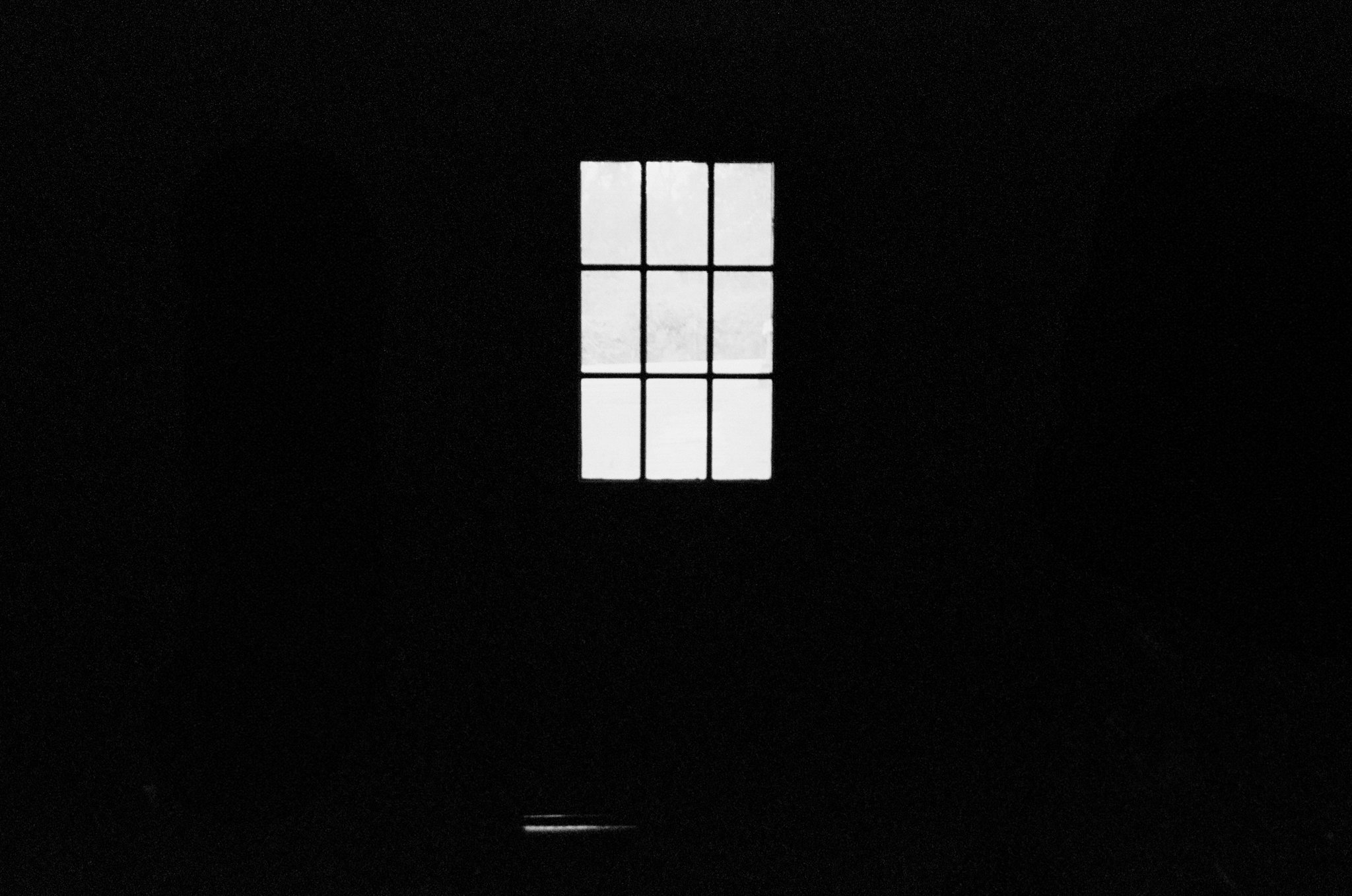 A small window with six panes is visible through a dark room, with bright light shining through the window.