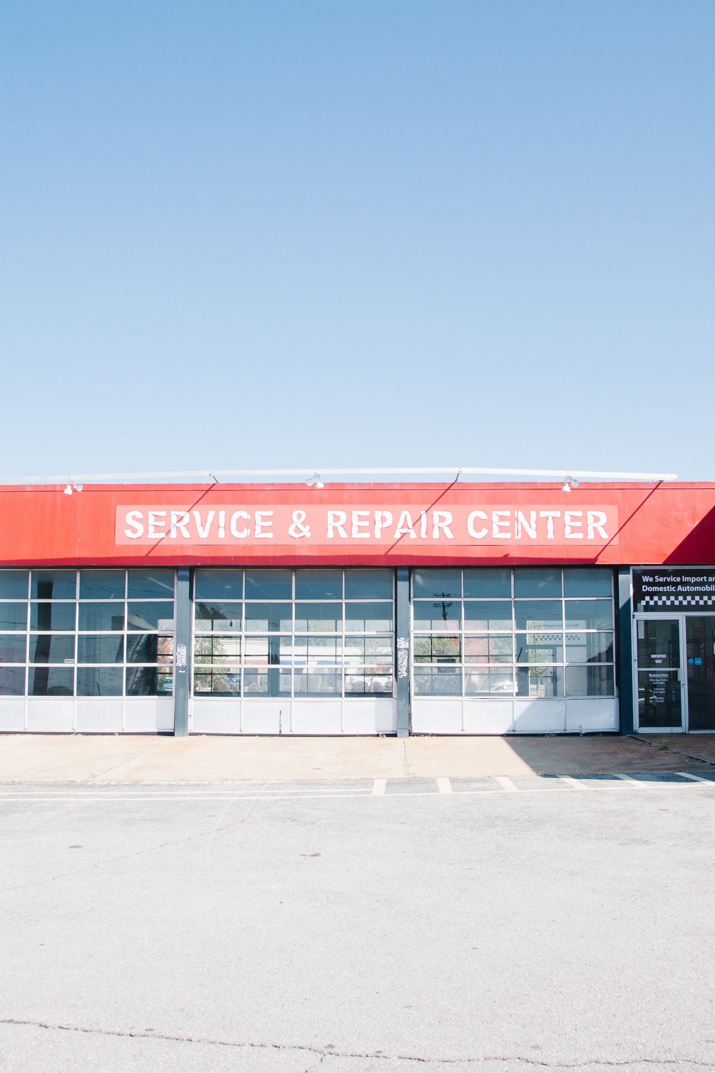 An exterior view of a service and repair center with large glass windows and a red sign above saying 'SERVICE & REPAIR CENTER' against a clear blue sky.