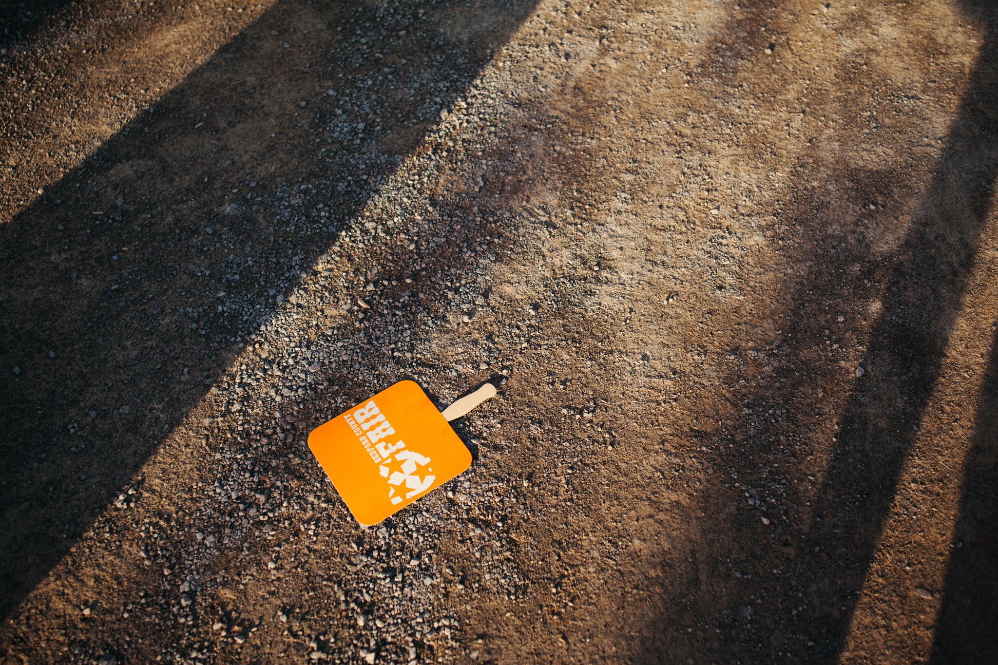 A bright orange sign with white text and stars lying on the ground, partially covered by gravel and dirt.
