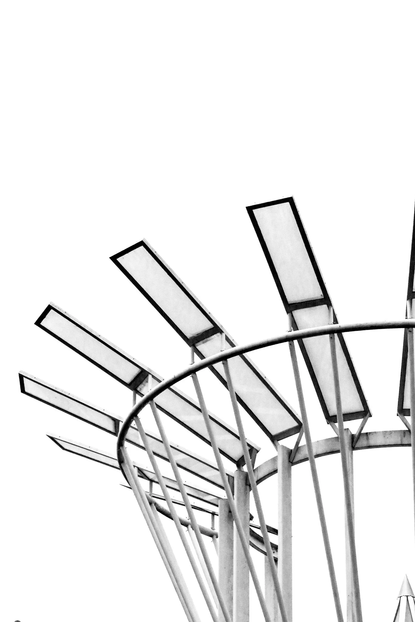 Close-up of a modern Ferris wheel with rectangular gondolas in black and white, focusing on the upper part of the structure against a cloudy sky.