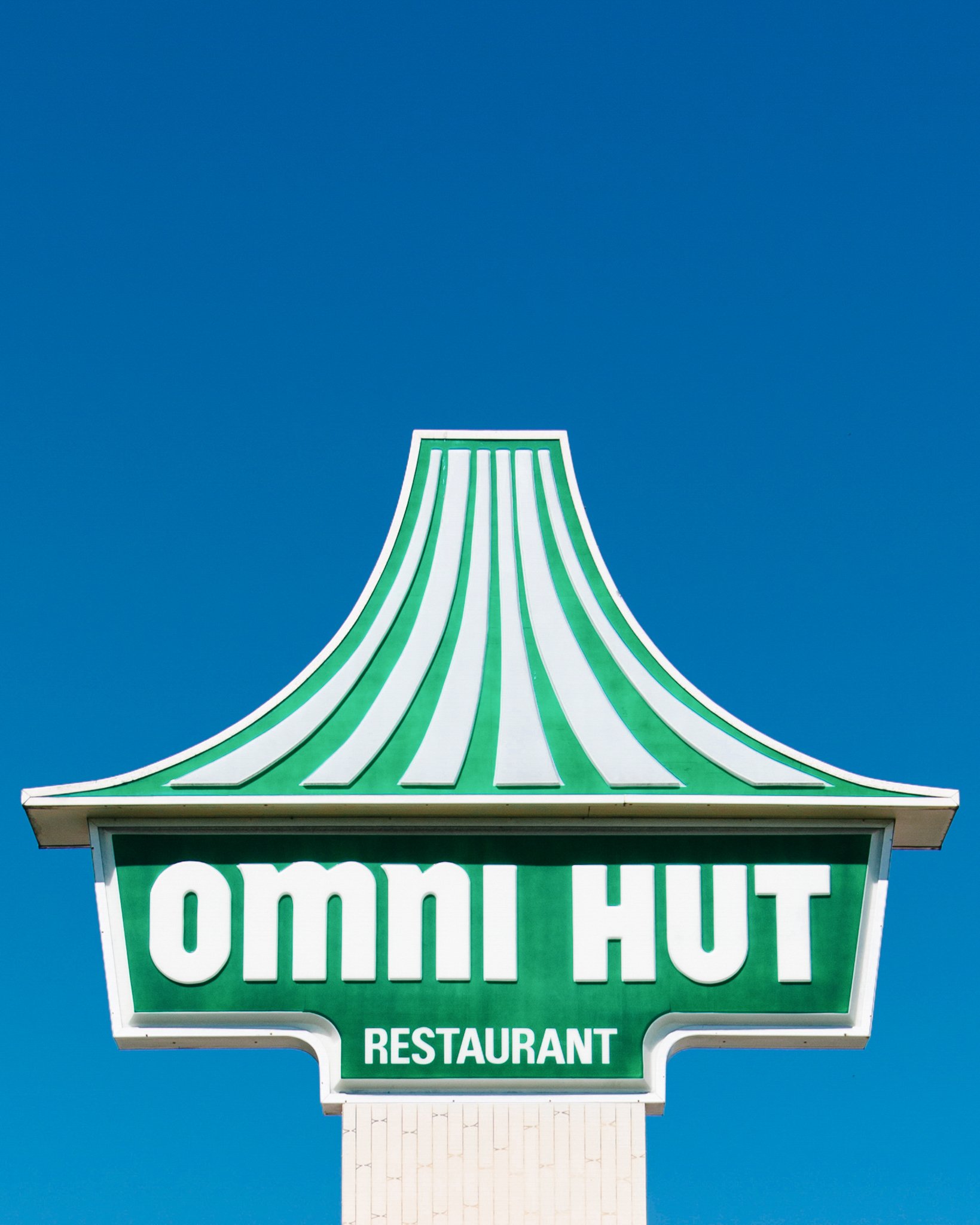 Close-up of a vintage drive-in restaurant sign with a green and white striped canopy, blue sky background, and the word 'COMMUNITY' visible at the bottom.