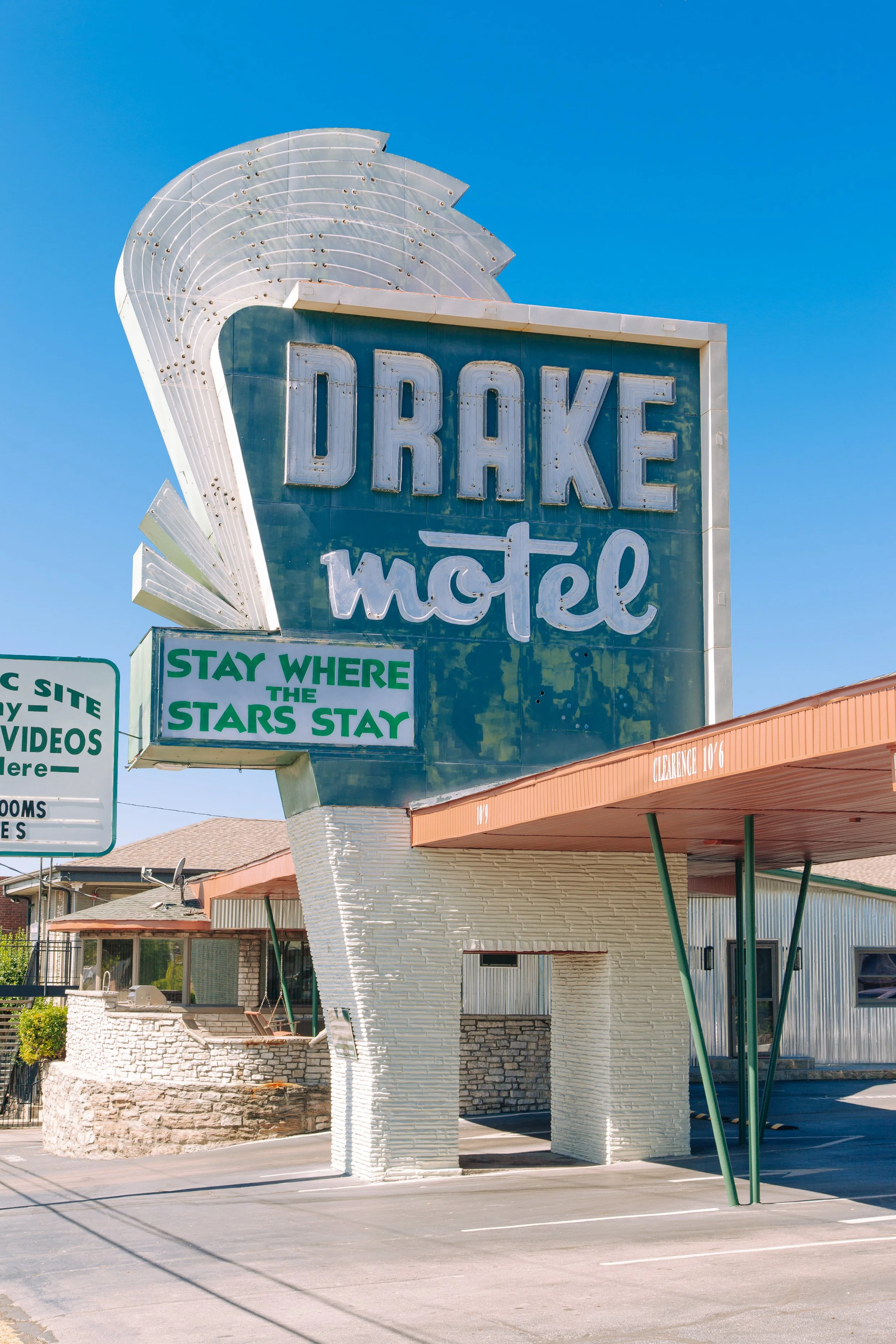 Vintage motel sign reading 'DRAKE motel' with a large decorative white arrow and blue background, under a clear blue sky.