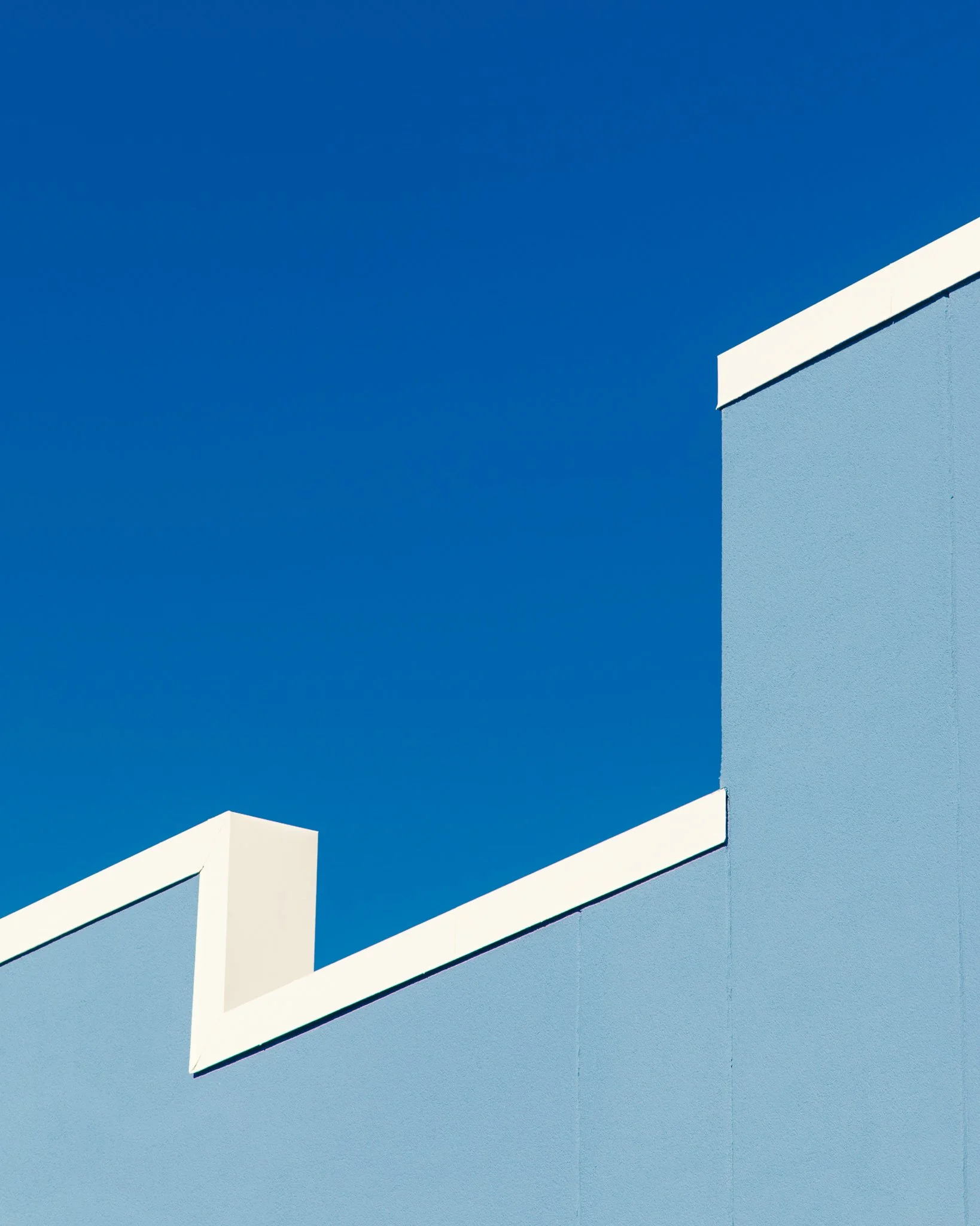A modern building with a light blue facade and white trim, against a clear blue sky.