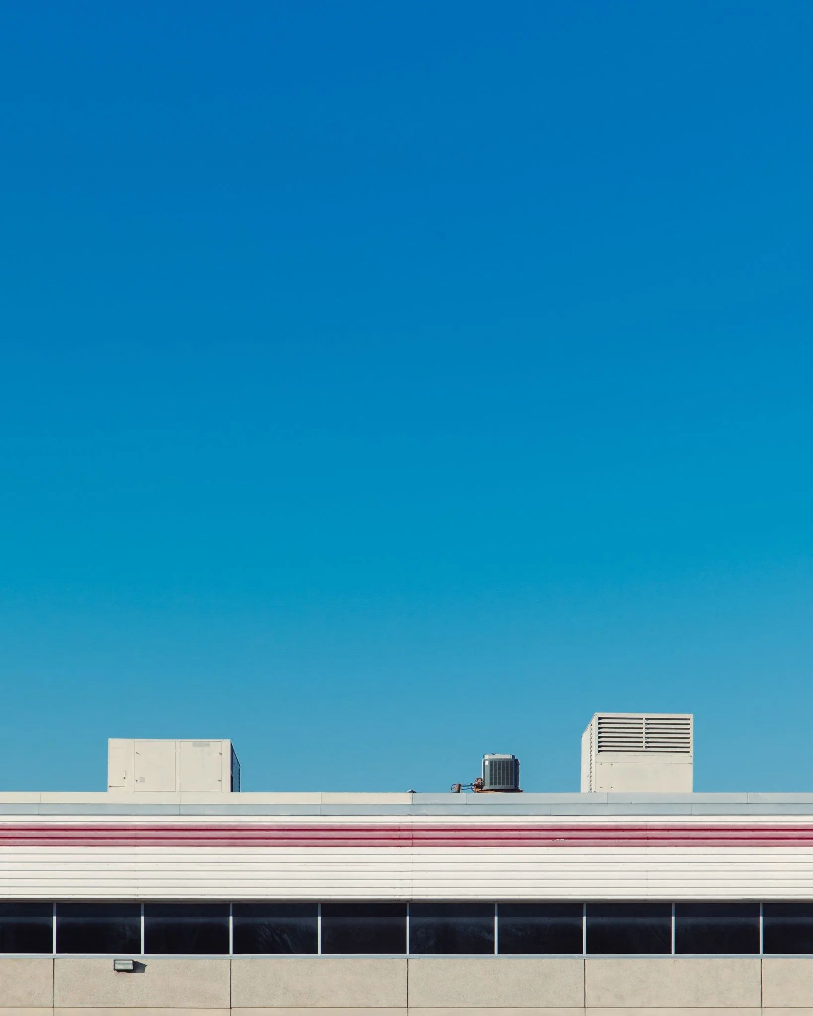 Photo of a building rooftop with HVAC units and ventilation systems against a clear blue sky.