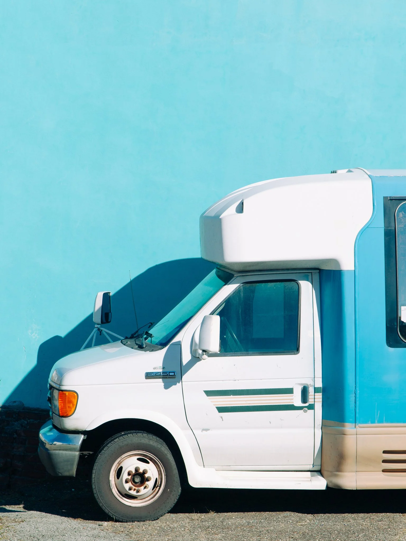 Side view of a white delivery truck with a blue cargo container against a blue wall.