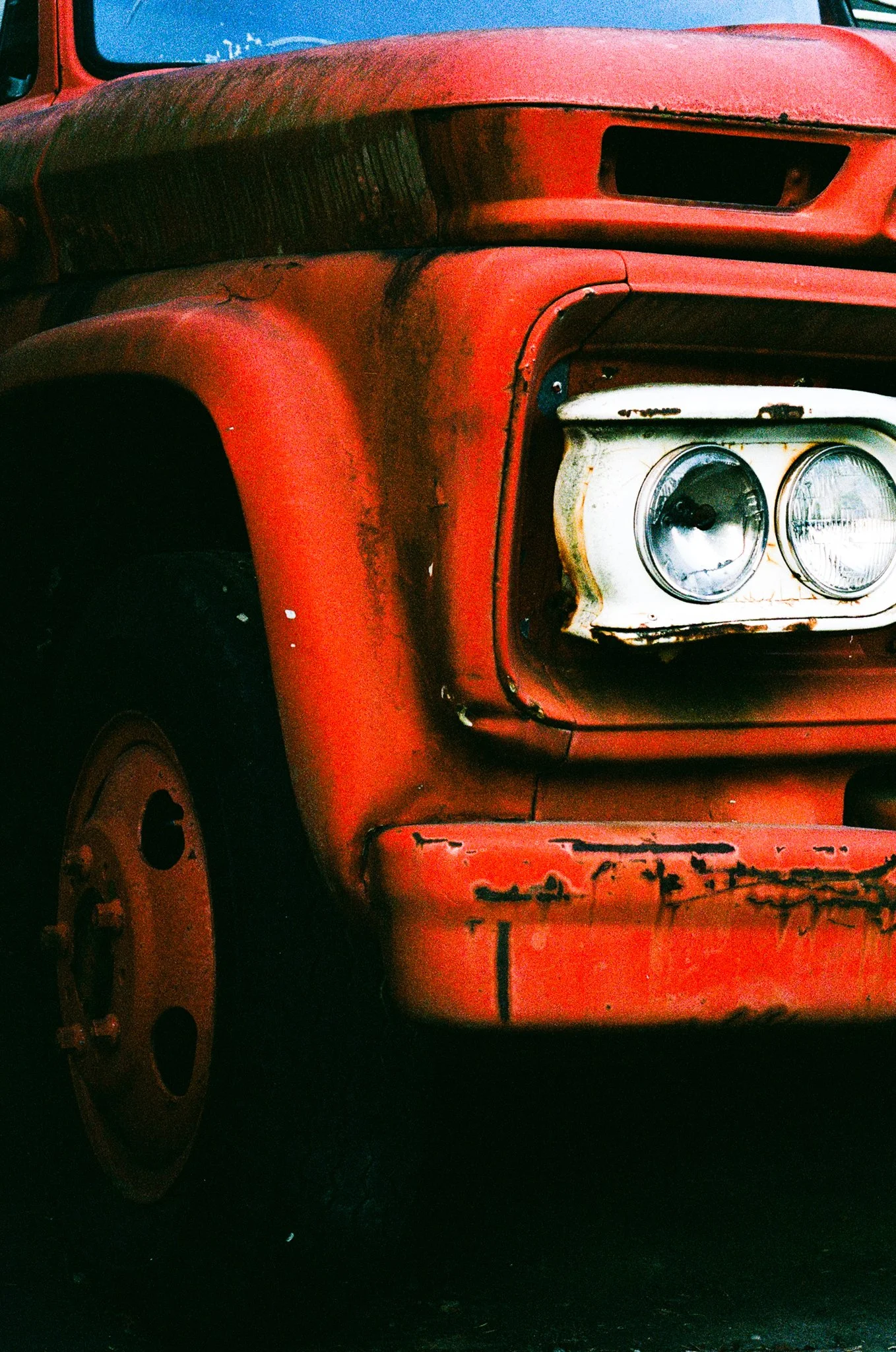 Close-up of an old, red vehicle with rust and wear, showing part of the front fender and headlight area.