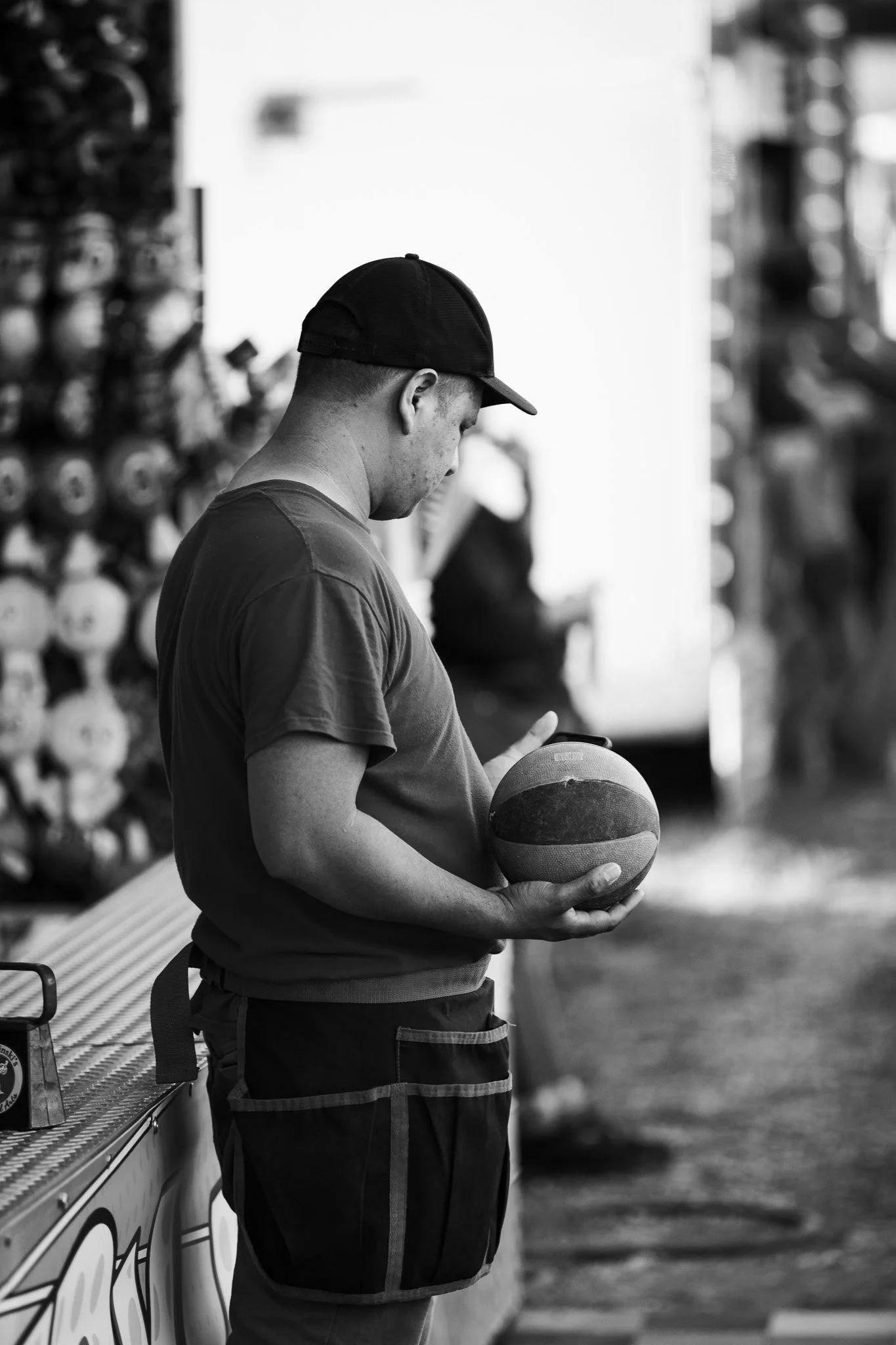 A man wearing a baseball cap and sports shorts is looking down at a basketball he is holding, standing next to a food truck.