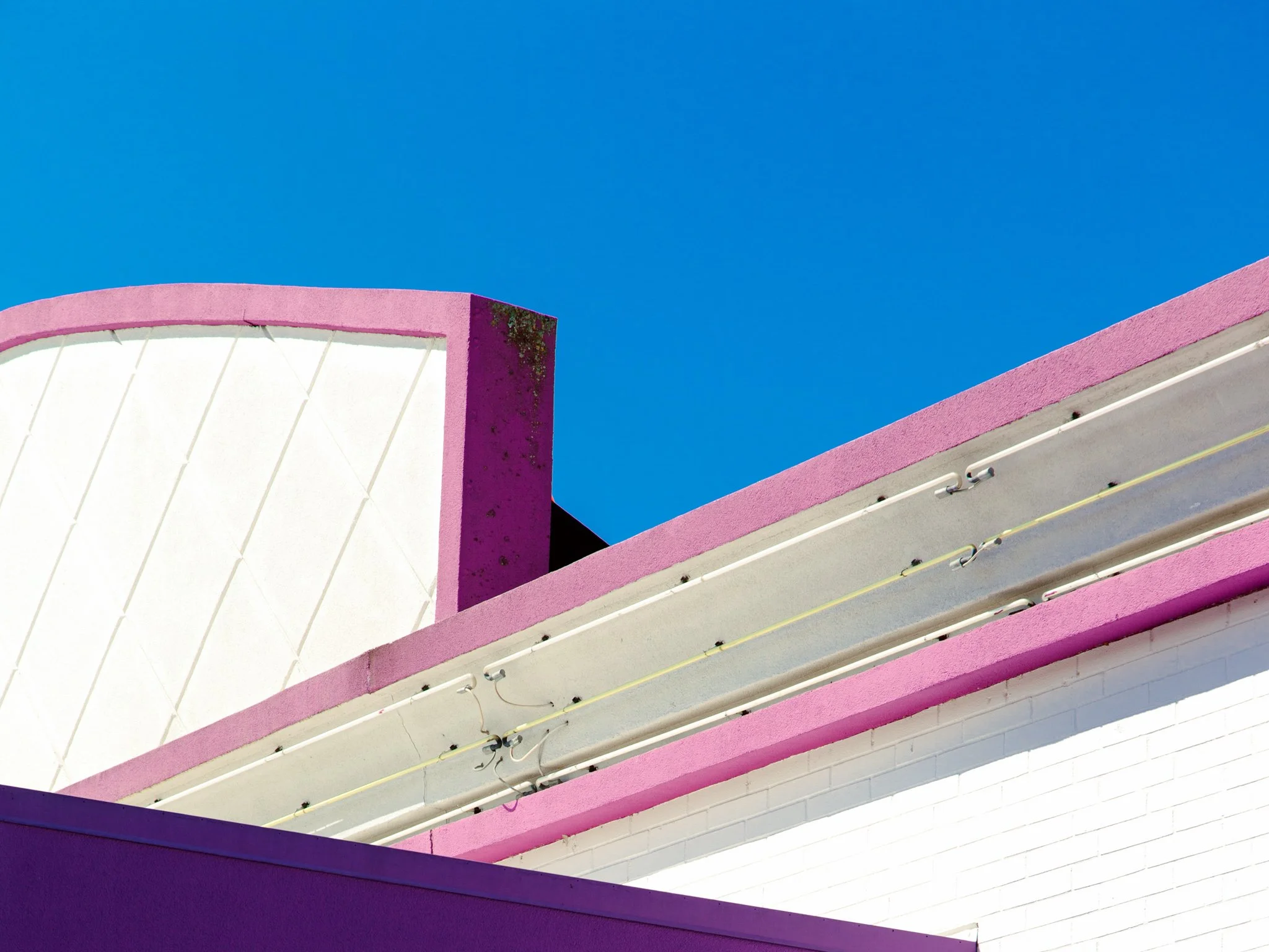 Close-up of a colorful building with pink and white walls, featuring curved architectural elements against a clear blue sky.
