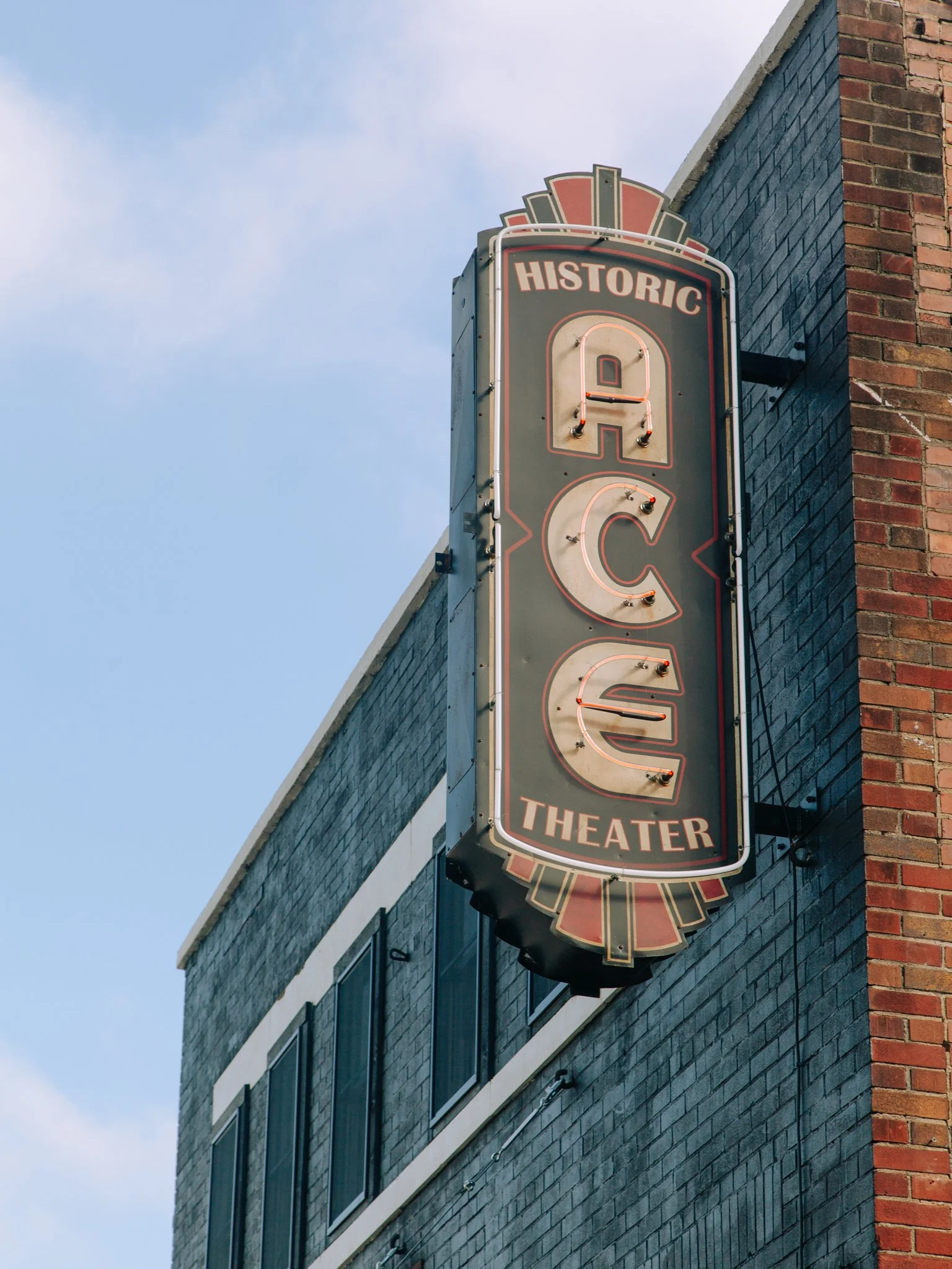Sign for the historic Queen Theatre mounted on the brick and black painted building exterior, with a blue sky in the background.