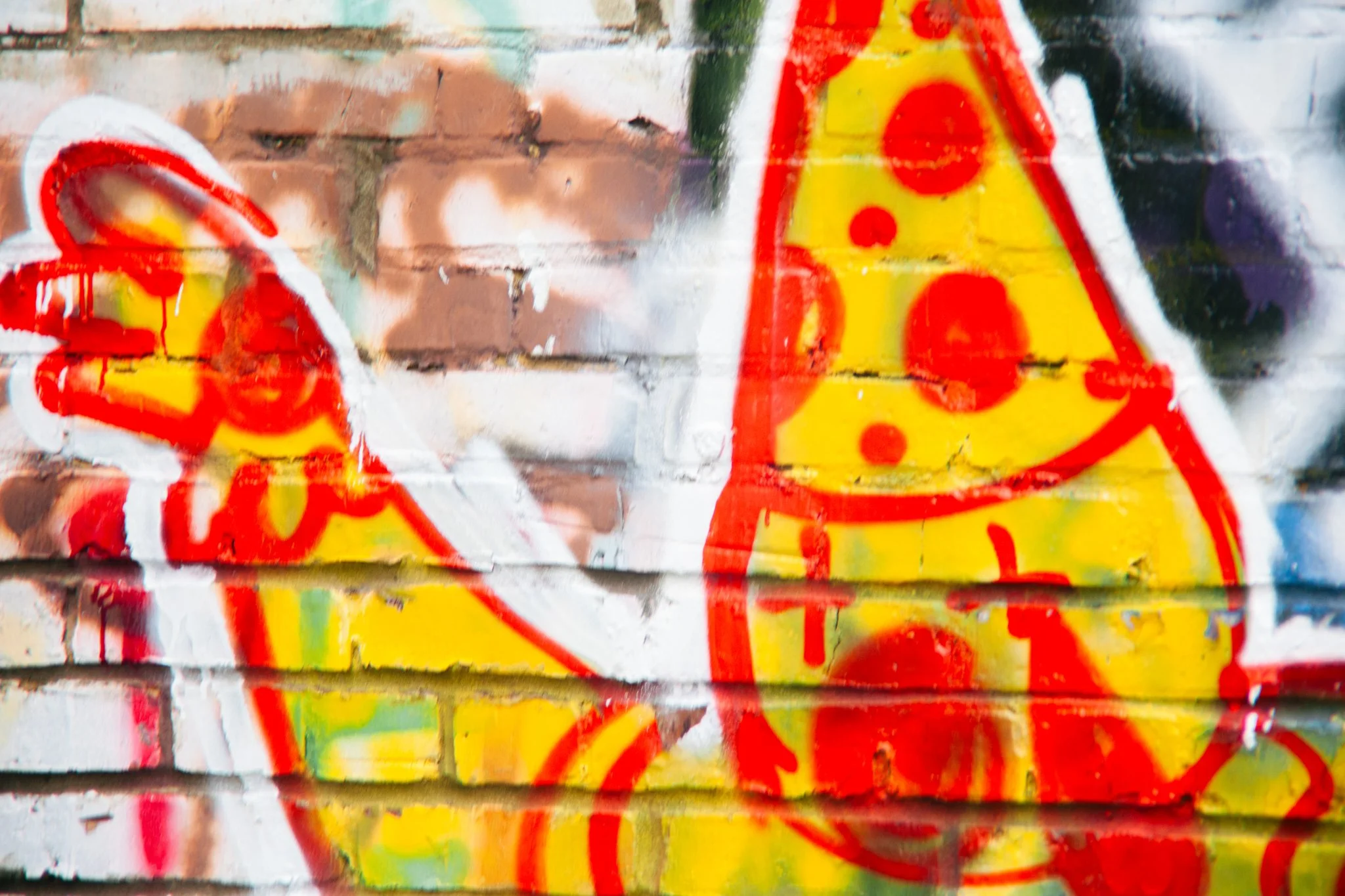 Close-up of colorful graffiti on brick wall featuring abstract red, yellow, and green shapes and lines.
