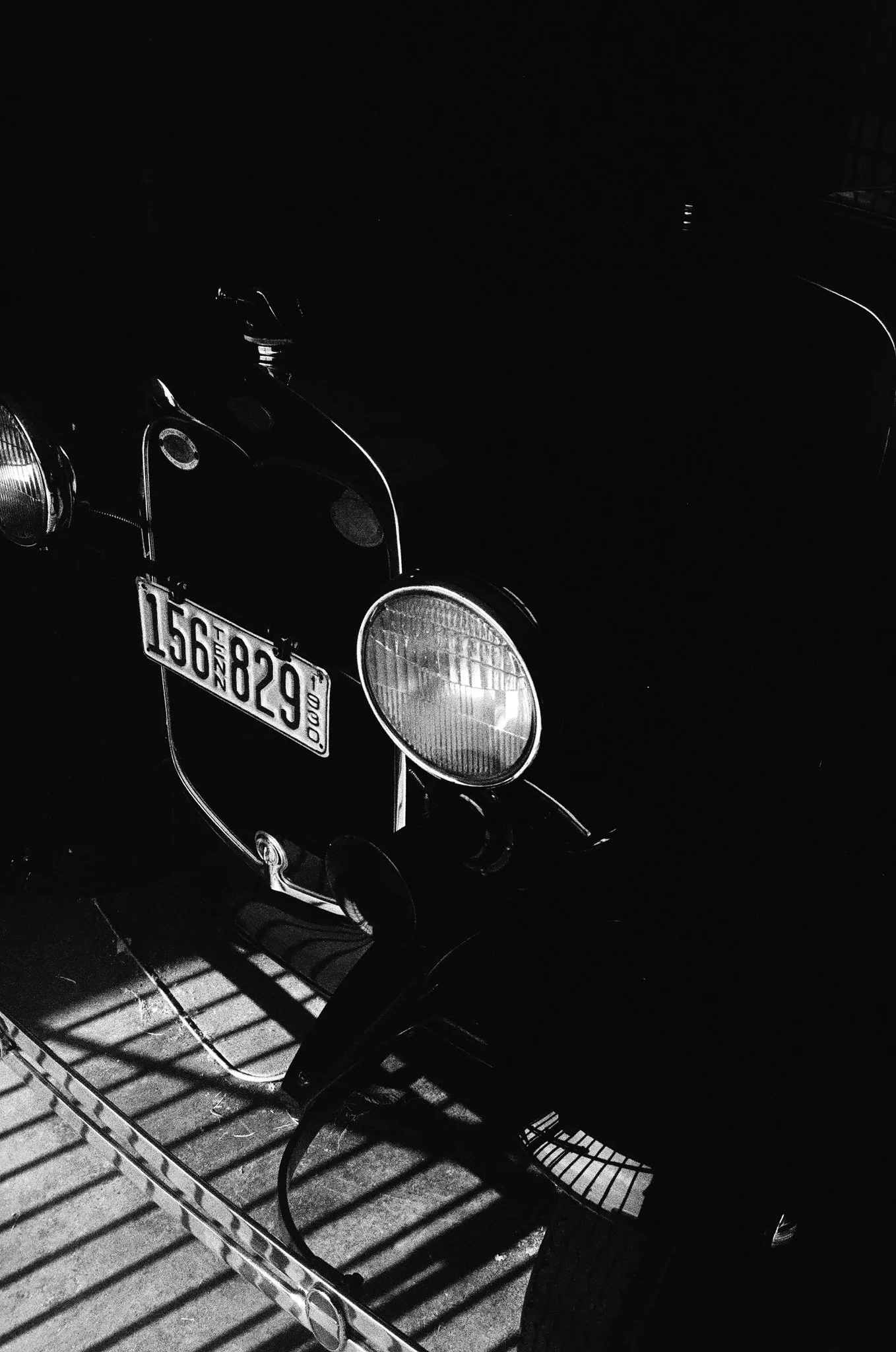 Black vintage scooter with headlight, parked on a tiled floor with shadows cast by a metal railing.