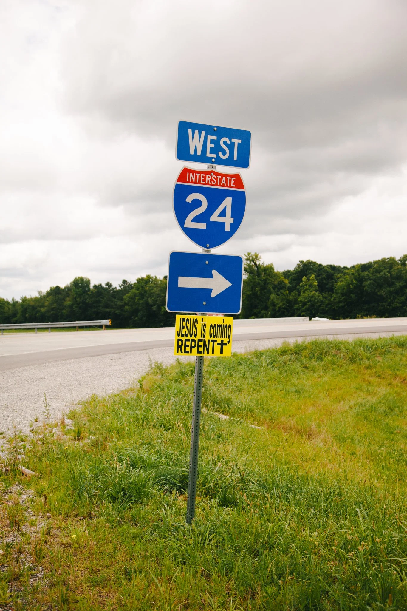 Highway road sign indicating west on Interstate 24 with a blue arrow pointing right, and a yellow sign below stating 'JESUS is coming REPEAT'.