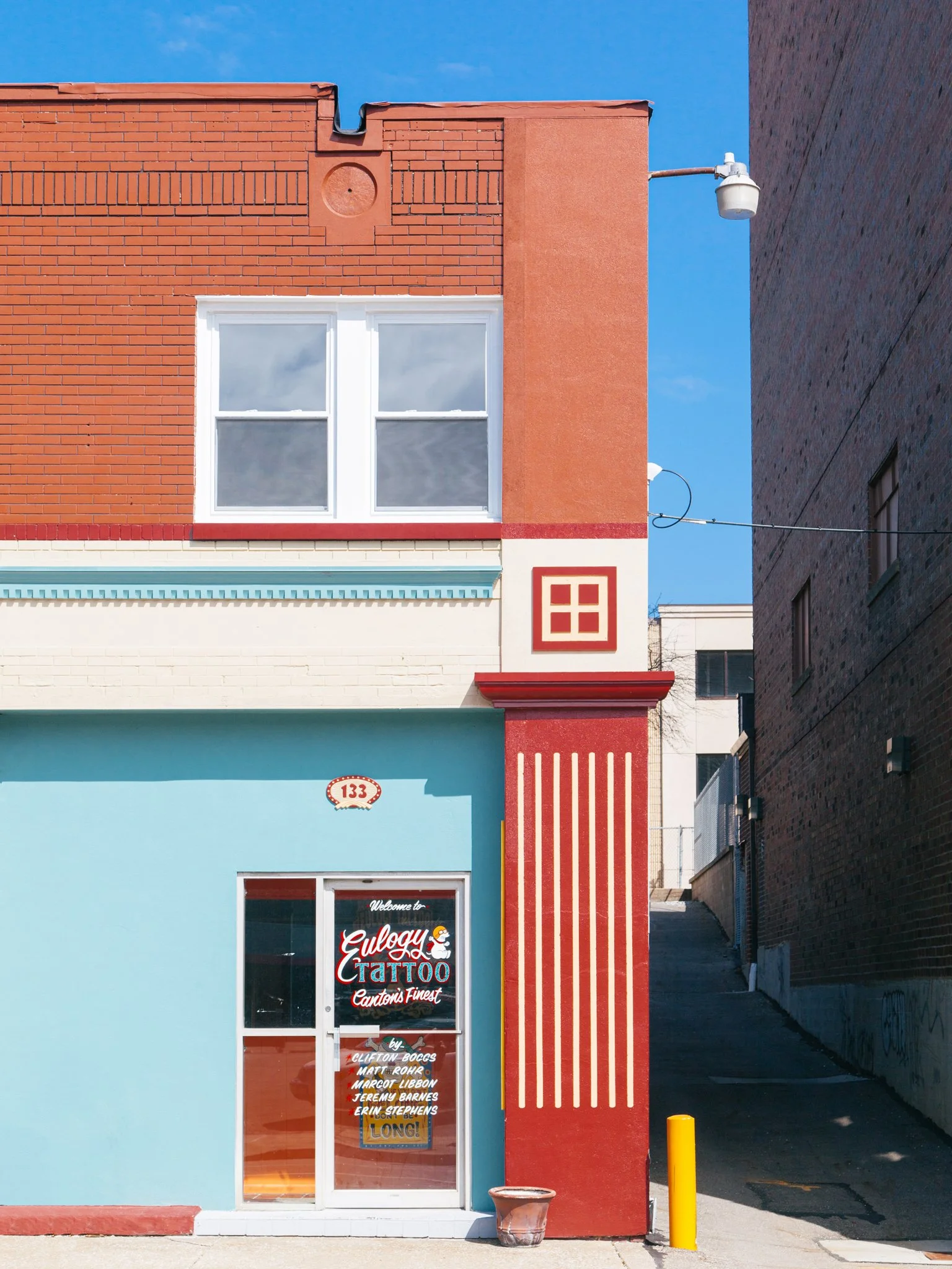 Colorful storefront with a blue wall, red and teal accents, and a glass door with tattoo shop sign.