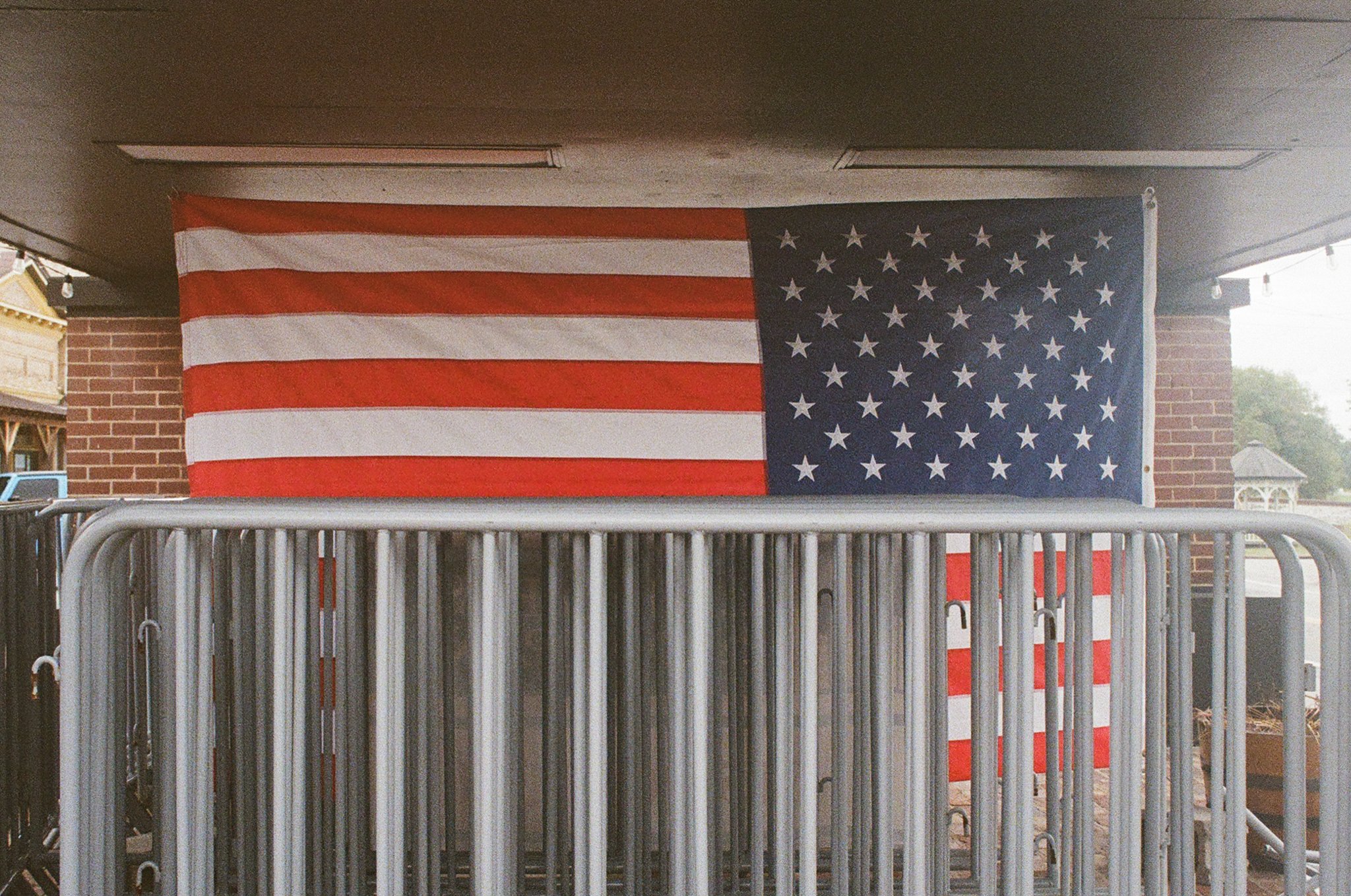 American flag hanging on a building near a brick wall and metal barriers.