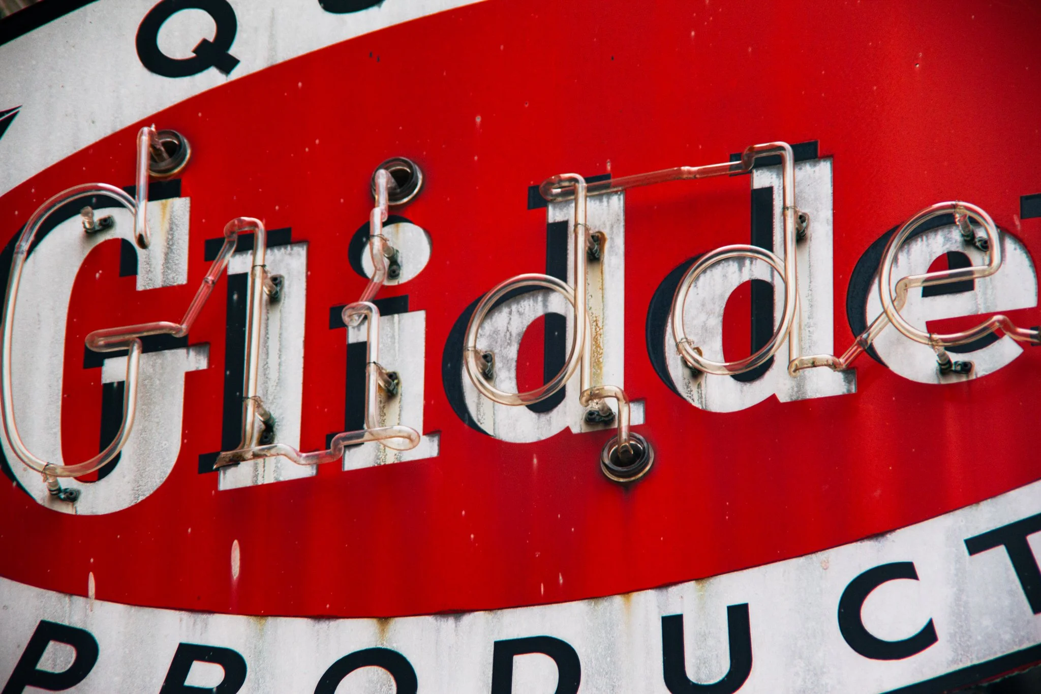 Close-up of a vintage sign with red and white background, featuring black letters and illuminated tubing lighting part of the sign.
