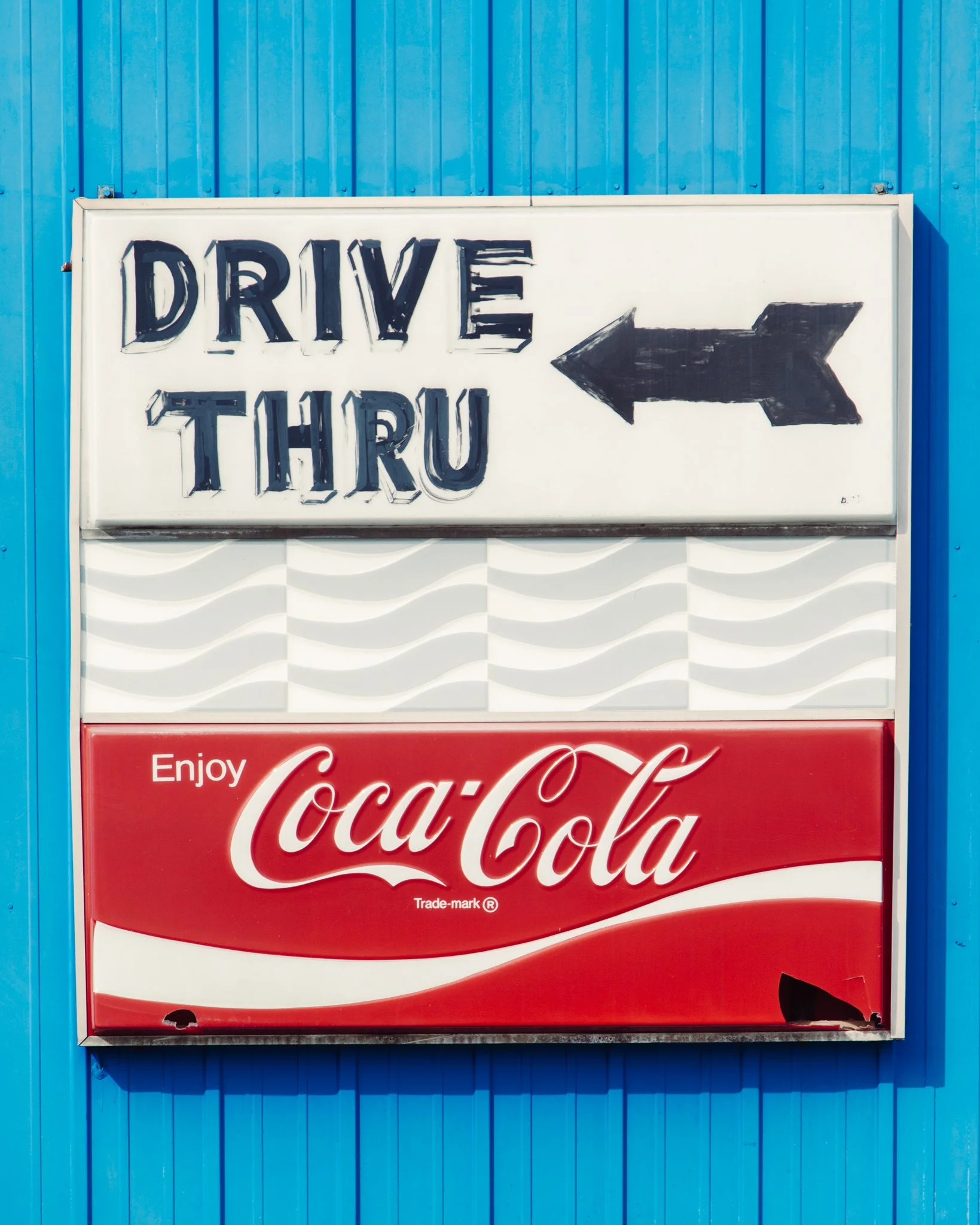 A street sign with the words 'DRIVE THRU' and an arrow pointing to the right, installed on a wall painted in bright blue.