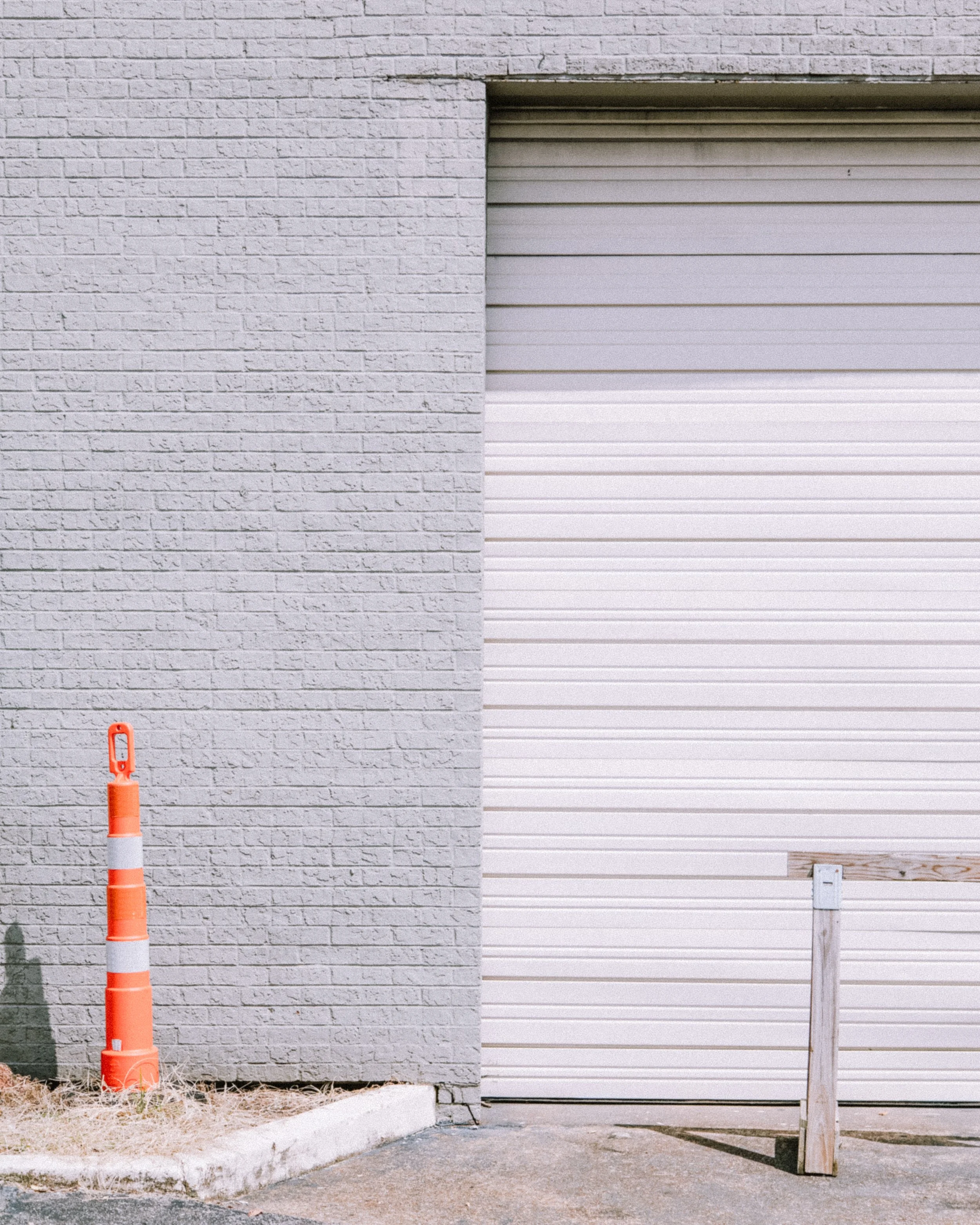 A garage door next to a brick wall with an orange and white traffic cone and a wooden post.