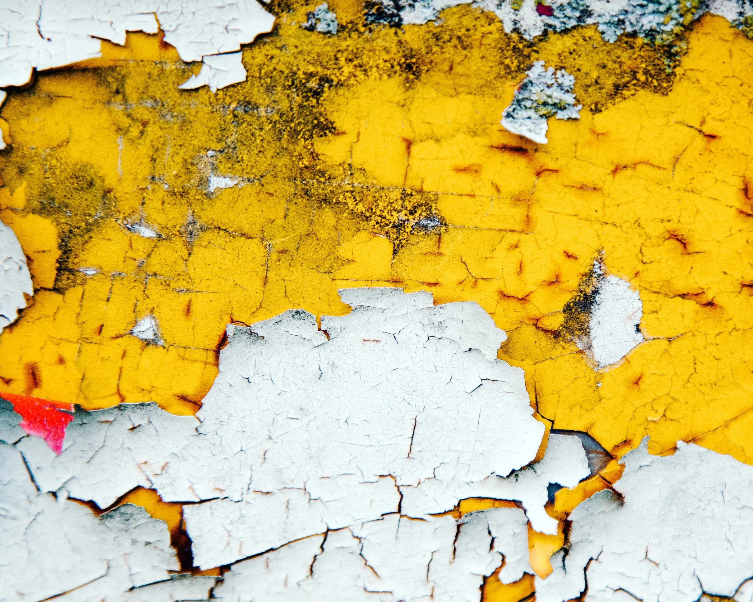Close-up of peeling yellow and white paint on a surface with cracks and chipped paint.