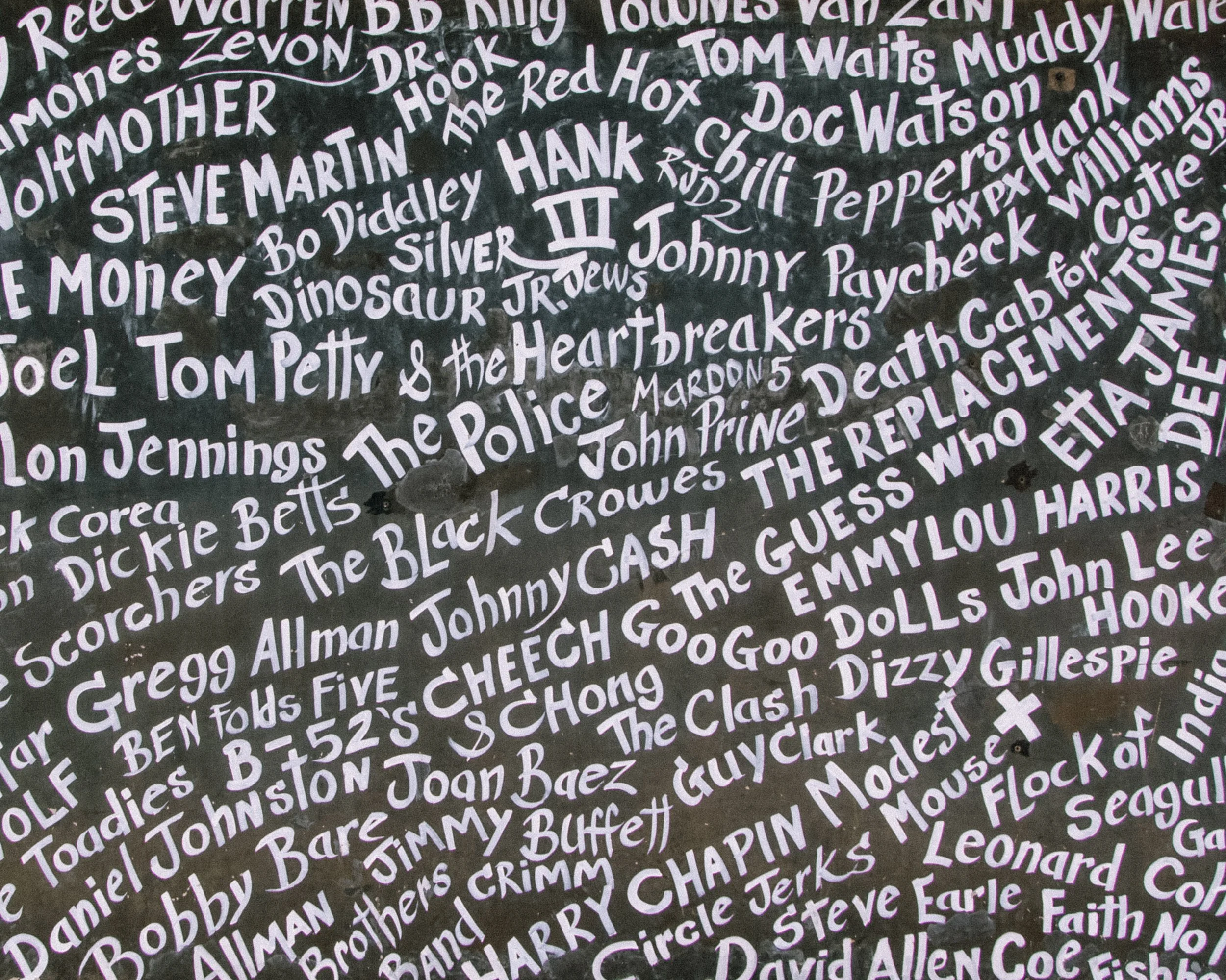 Close-up of a black surface covered with handwritten names in white, including notable figures like Steve Martin, Hank, Johnny Cash, and others.