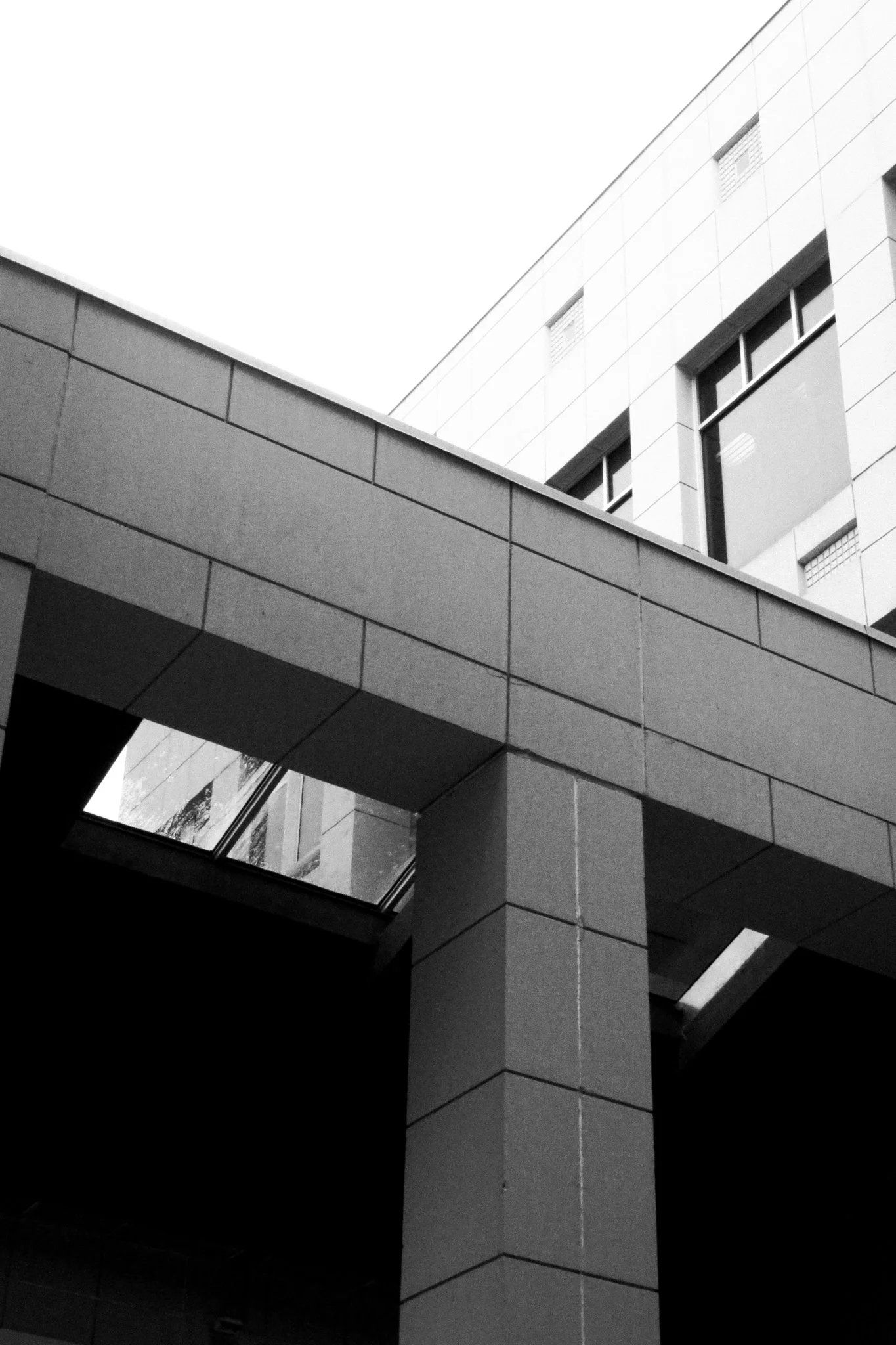 Black and white photograph of a modern building with angular architecture, featuring large windows, geometric shapes, and a mix of flat and angled surfaces.