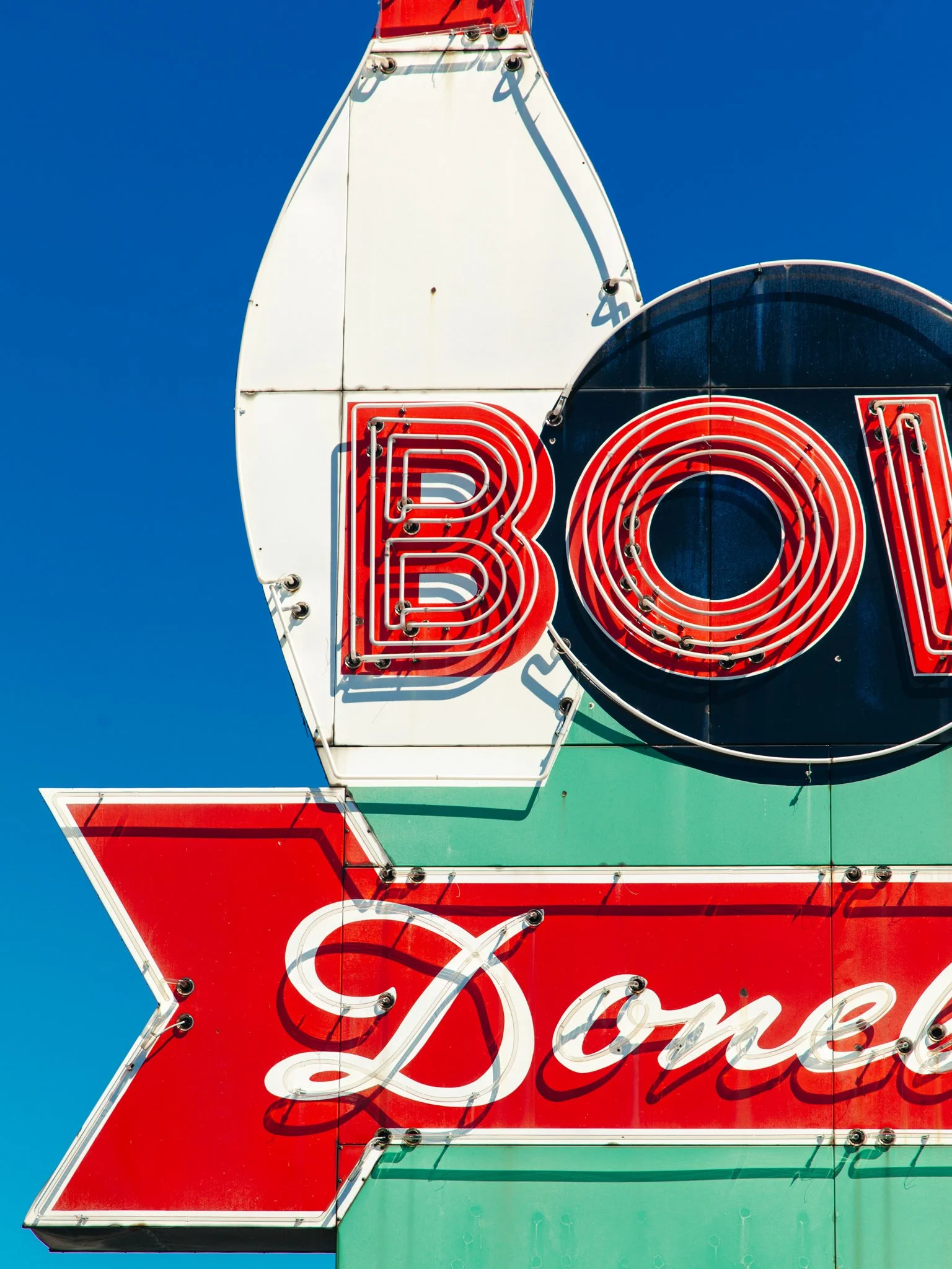 Close-up of a neon sign with the word "BAR" in red lights and part of the word "Coca-Cola" in white lights, against a clear blue sky.